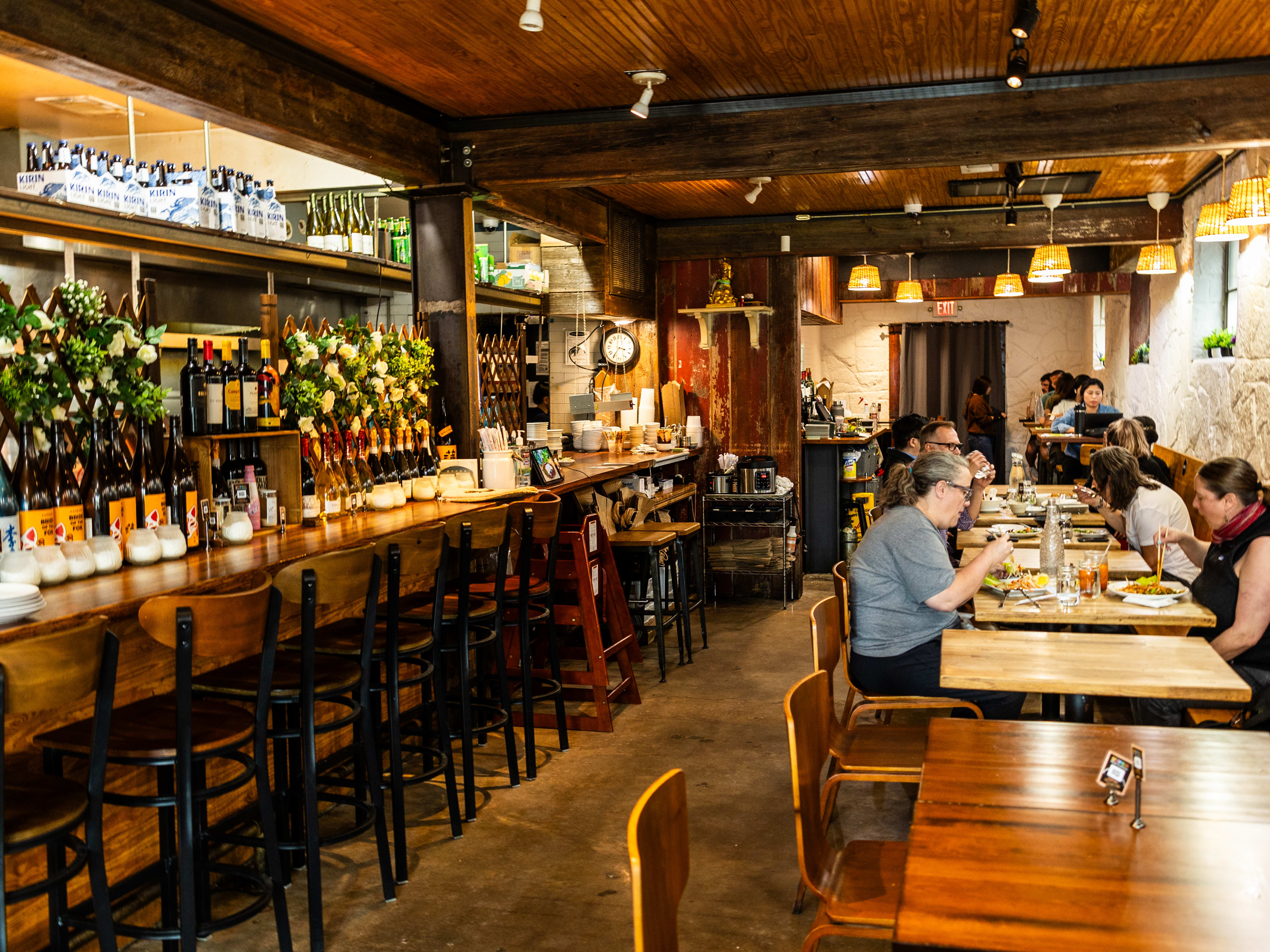 The interior of Super Thai with people eating tables at a long booth. Foliage covers trellises on the back of the bar to the left.