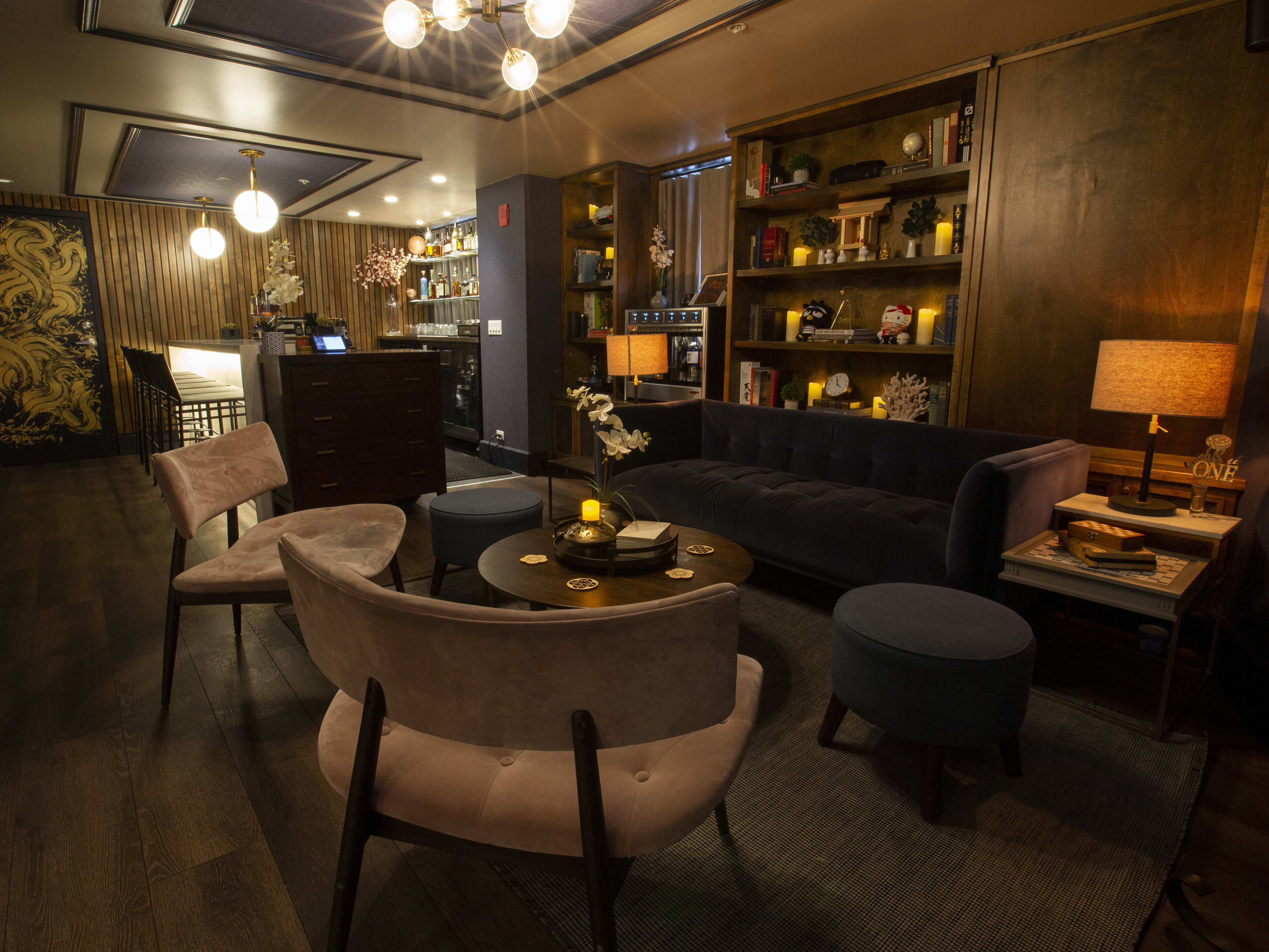 Lounge seating with a couch, ottomans, velvet chairs, and wooden bookshelves in the background