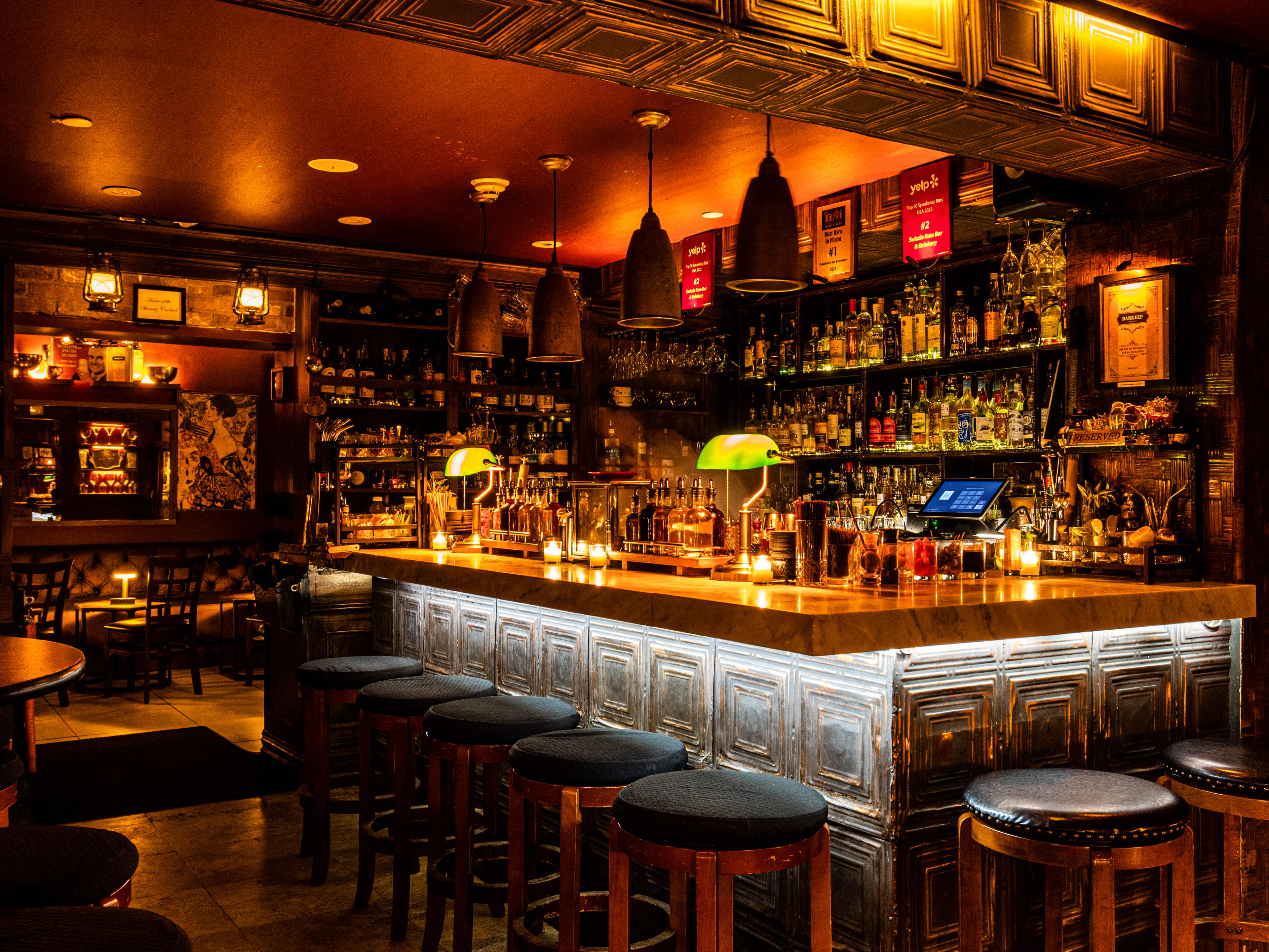 dark bar with liquor shelf, lamps on bartop, and warm lighting