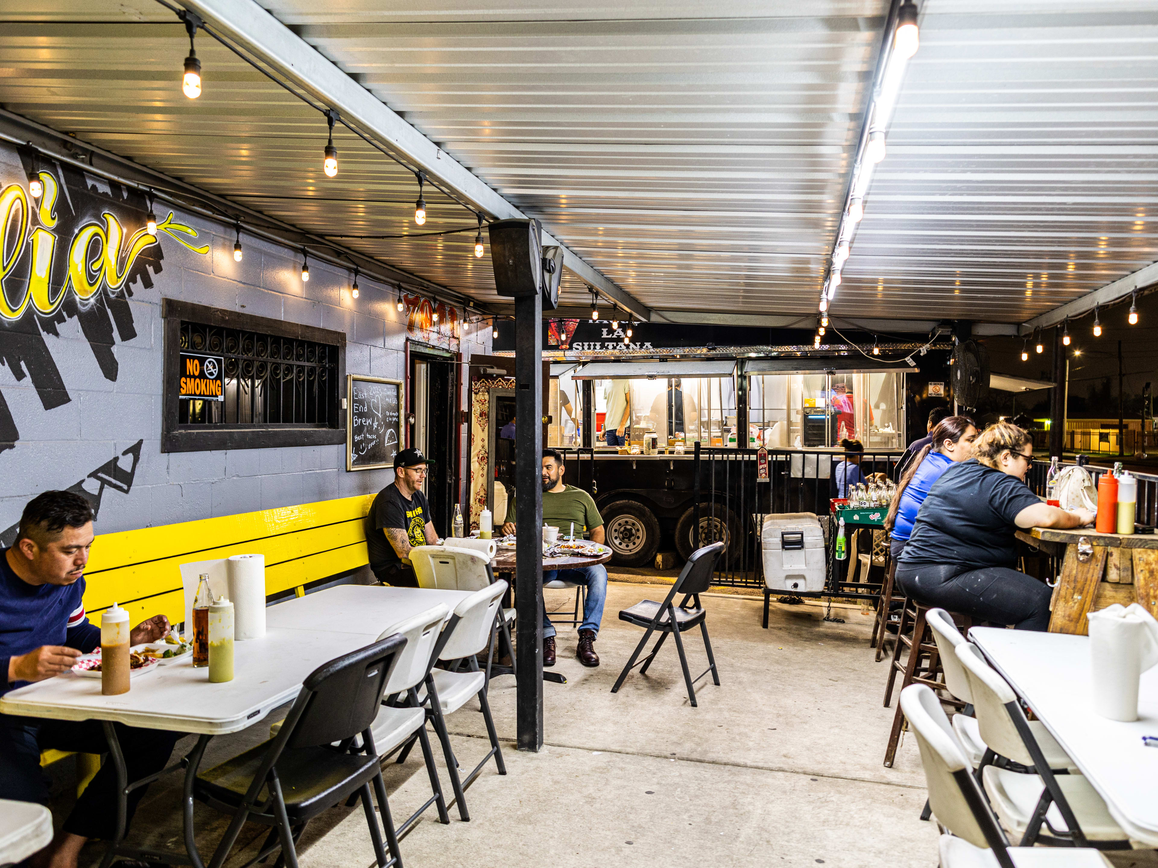 People eating at folding tables in a covered patio at Tacos La Sultana.