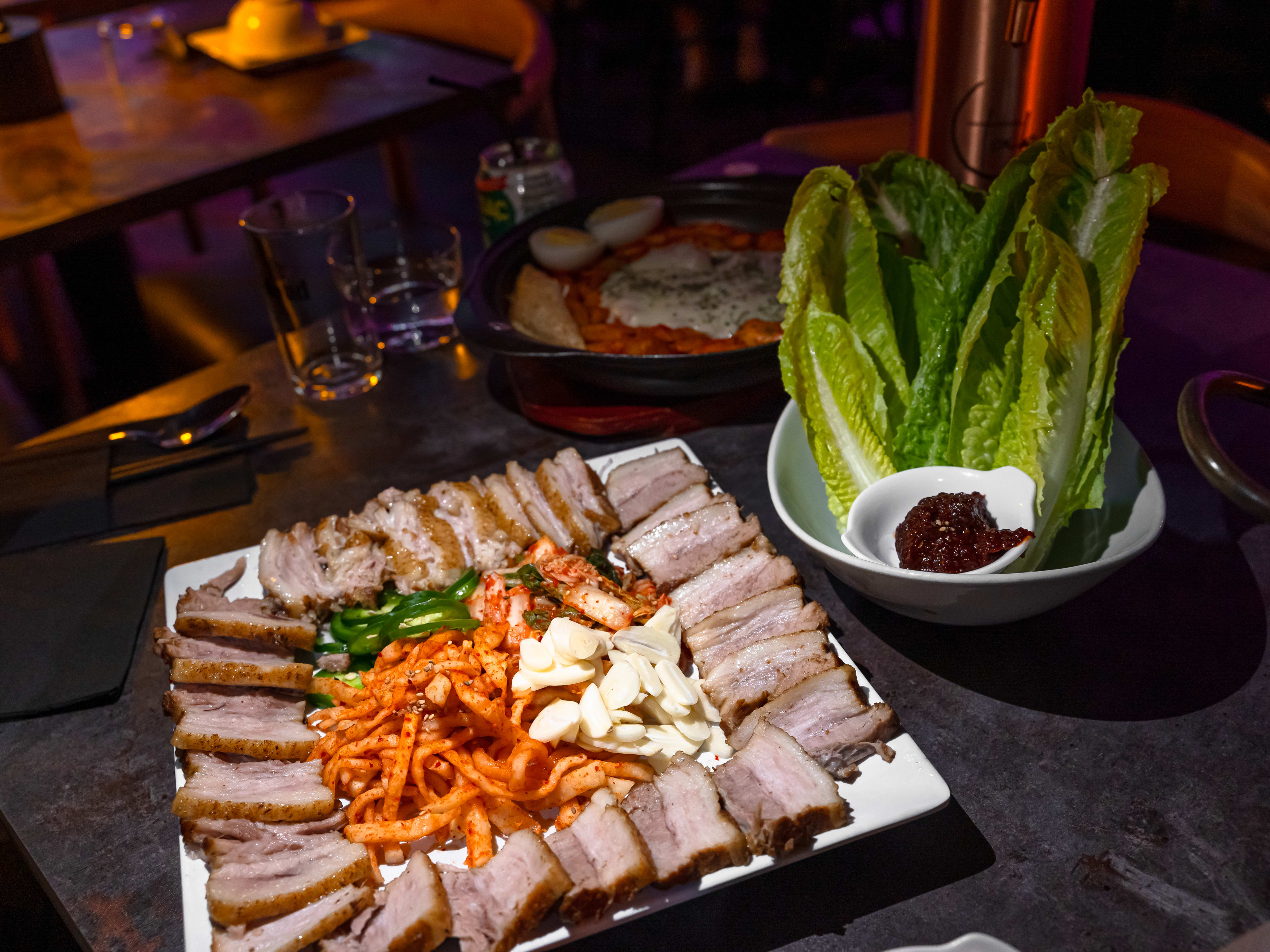 A plate of bossam with kimchi in the middle and a side of lettuce wraps.