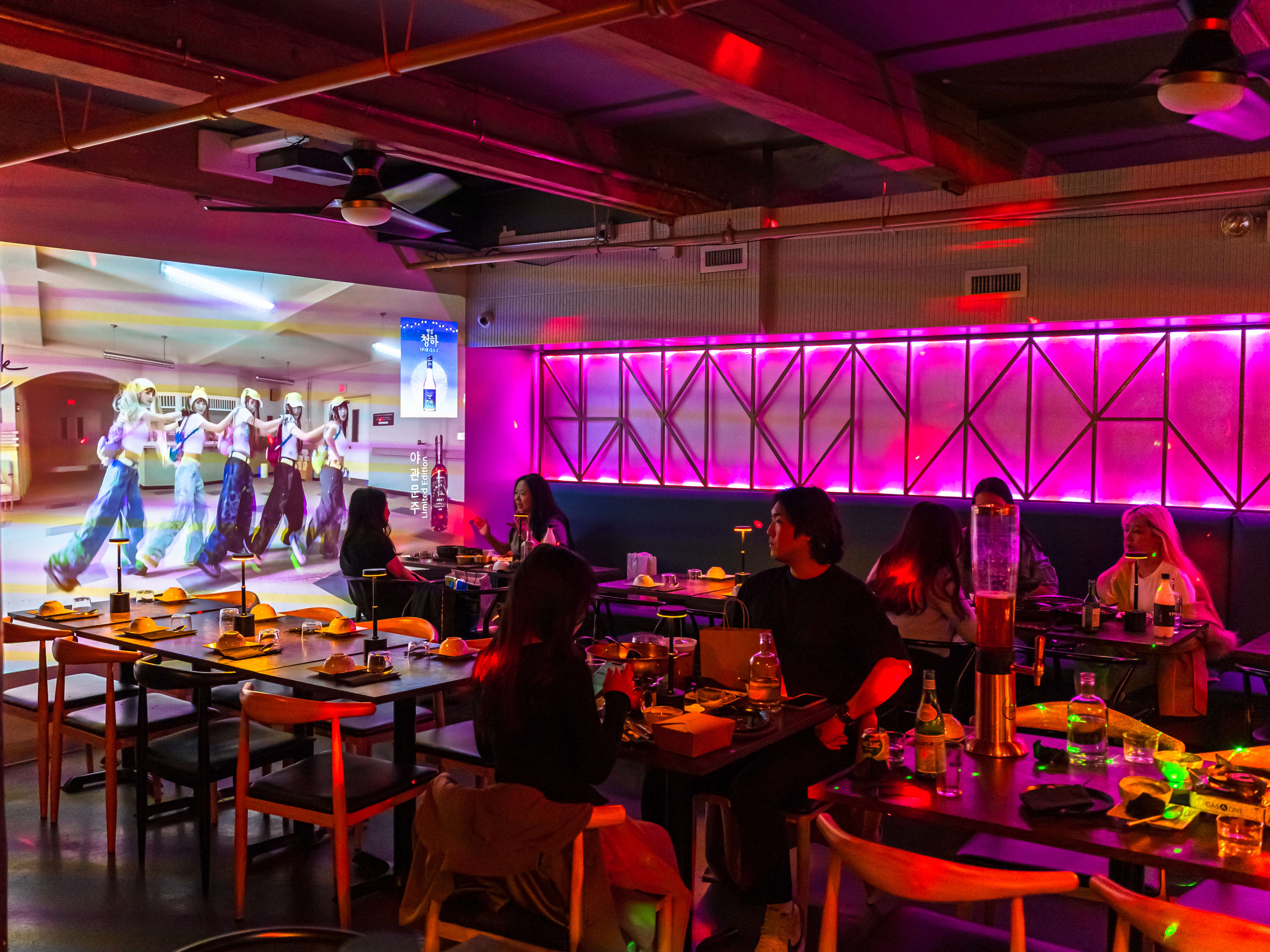 The neon lit interior of Tak Korean Bistro. A projector screen is playing music videos.