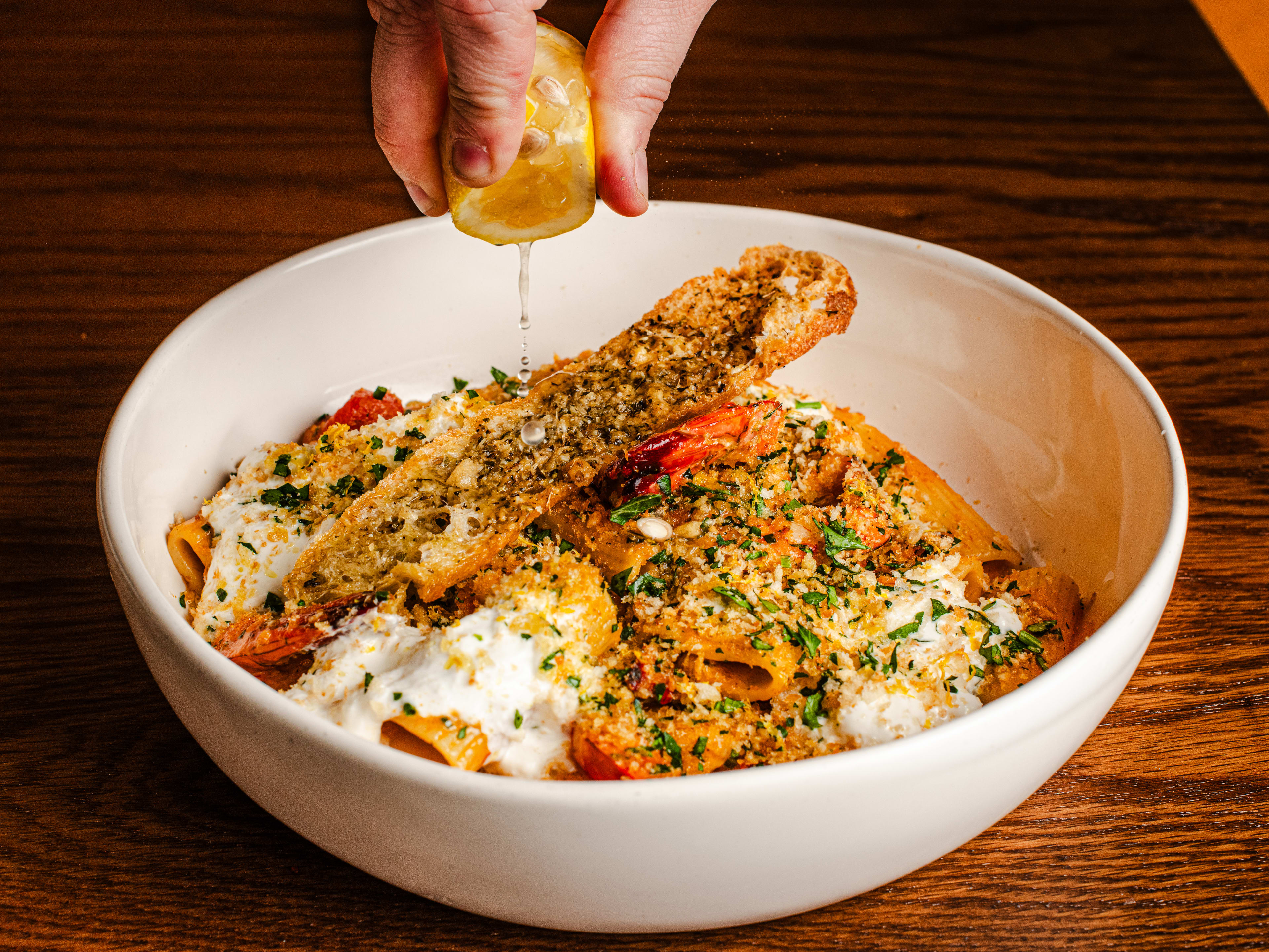 A lemon is squeezed over a bowl of prawn pasta.