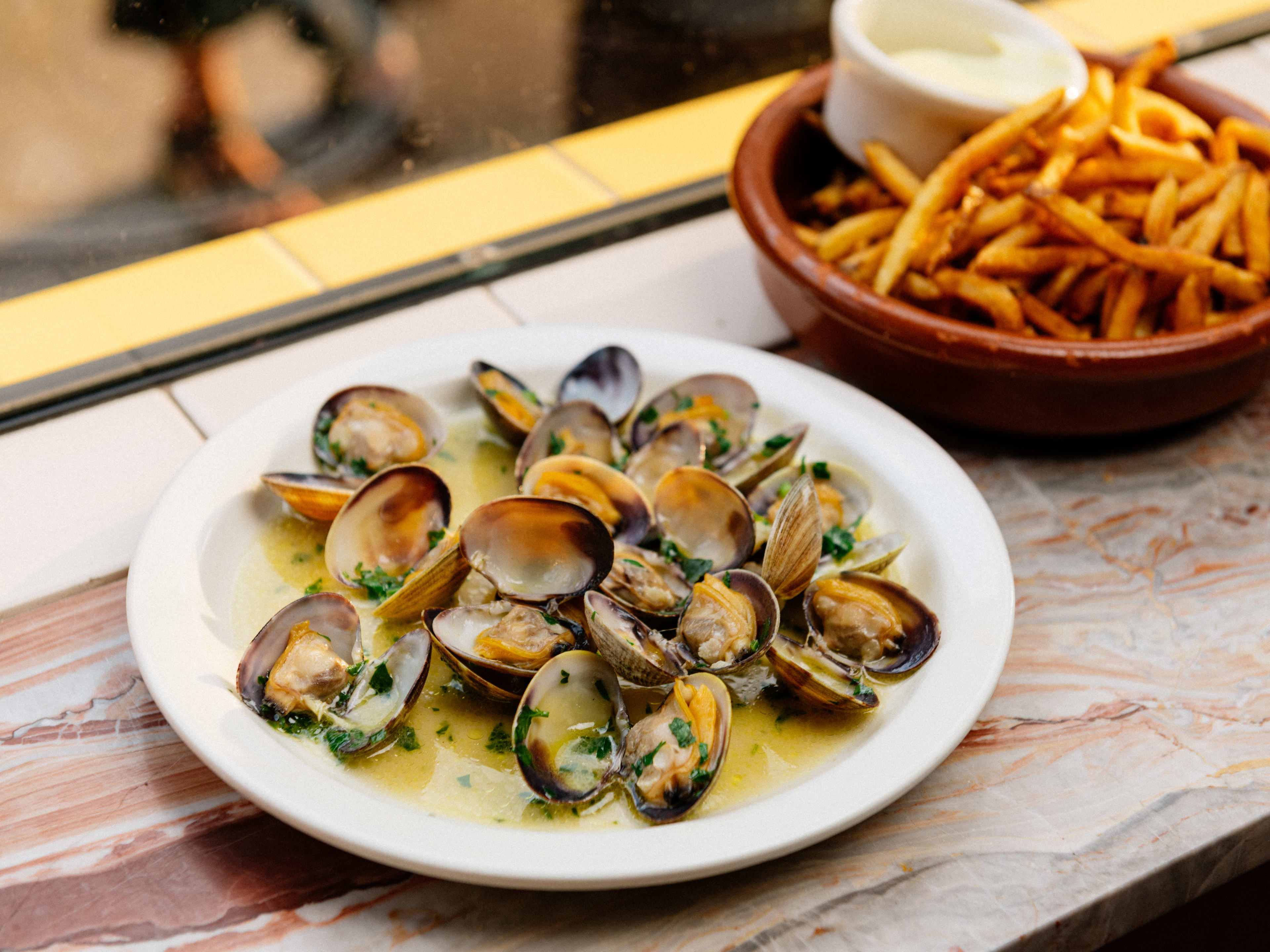 A small plate of manilla clams sitting broth, with a side of fries.