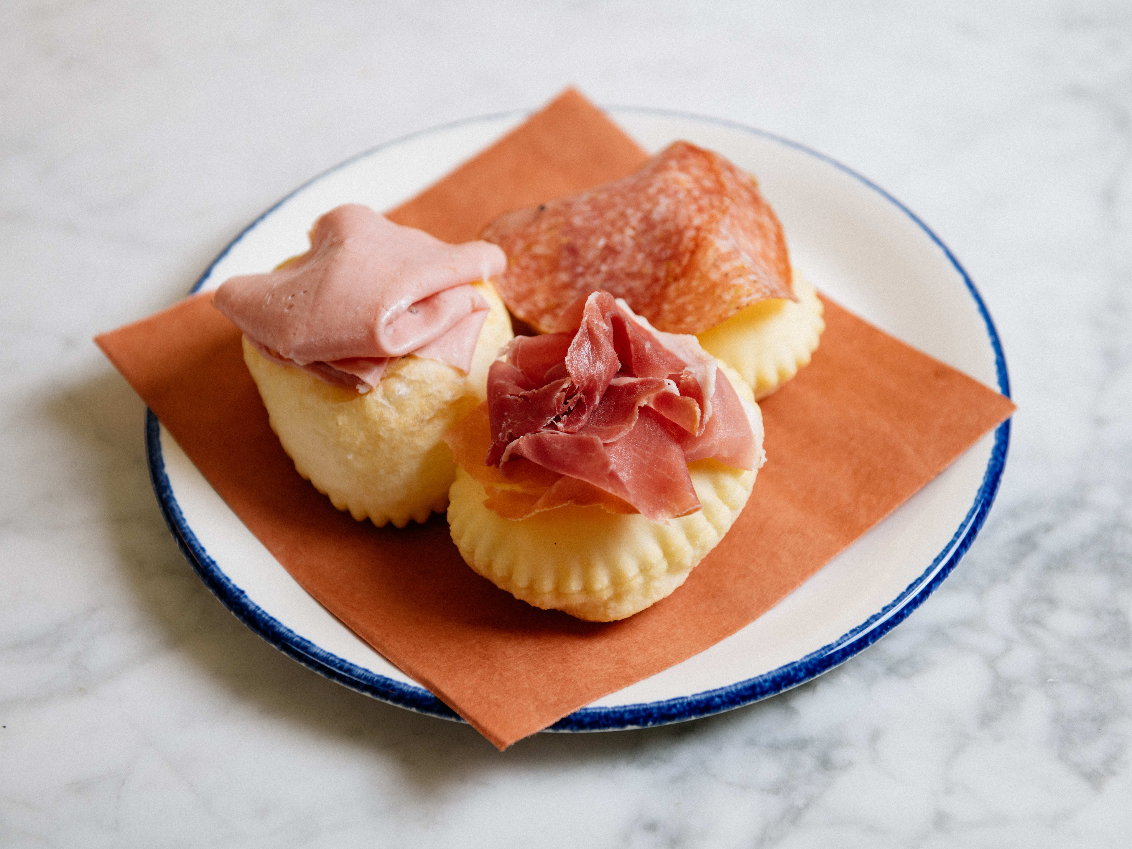 Three gnocco fritto topped with cured meat.