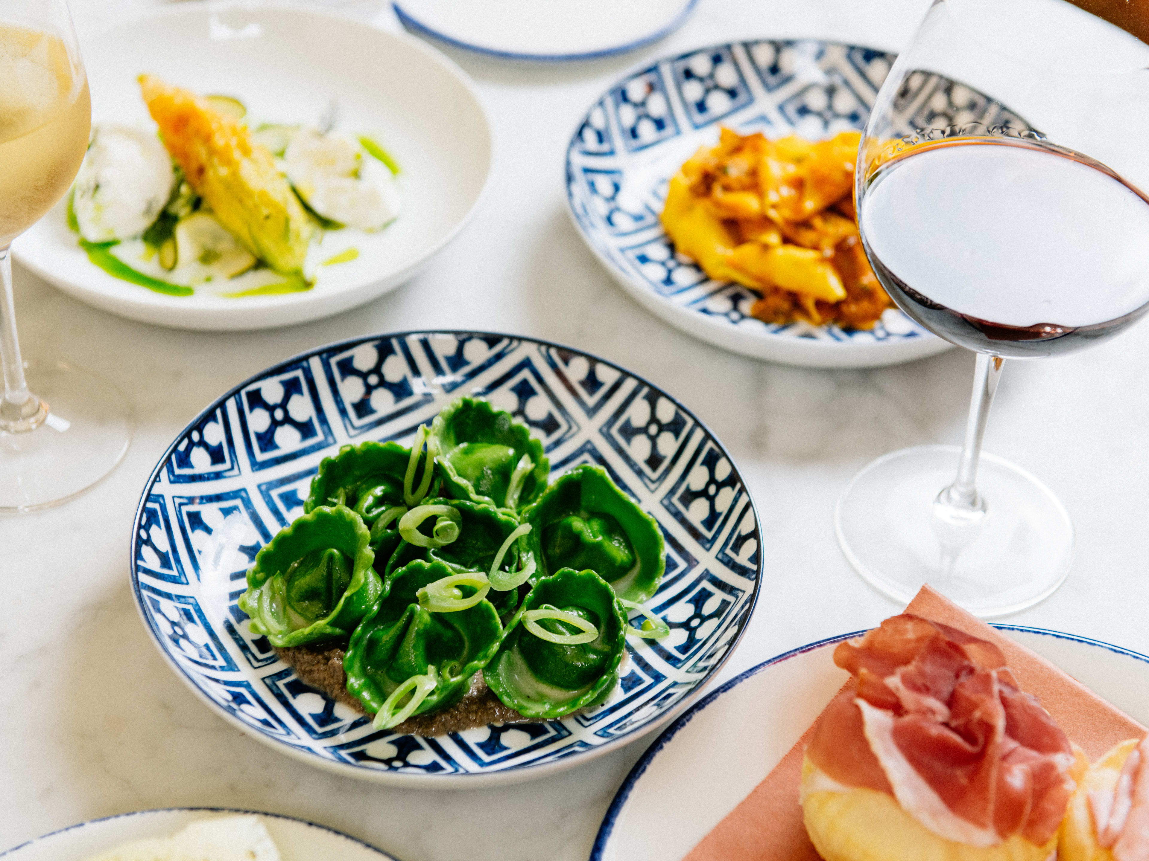 A few plates of pasta sitting next to some glasses of wine, with gnocco fritto on the side.