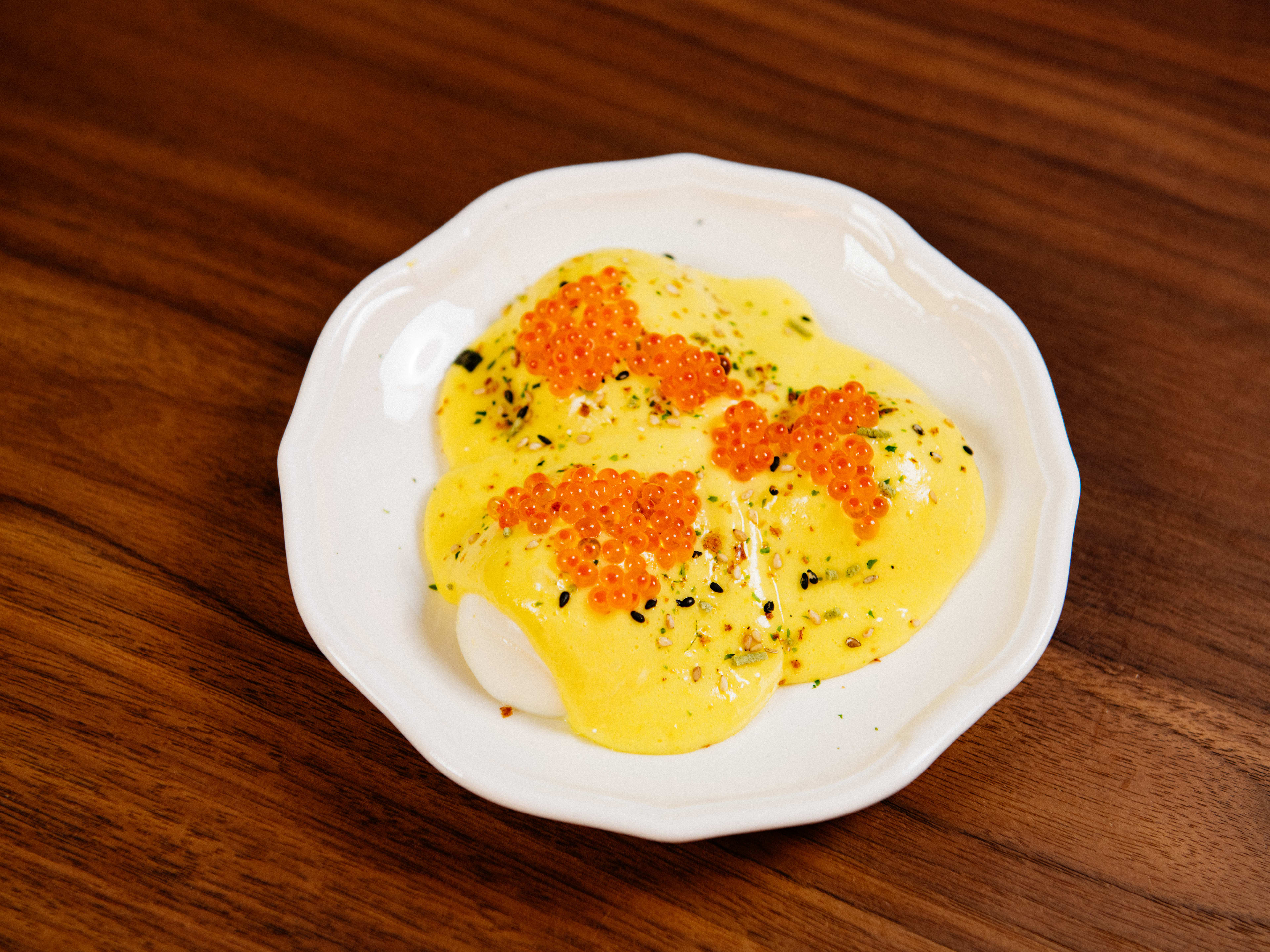 A small plate of boiled eggs smothered in a heavy, yellow mayo sauce with trout roe on top.