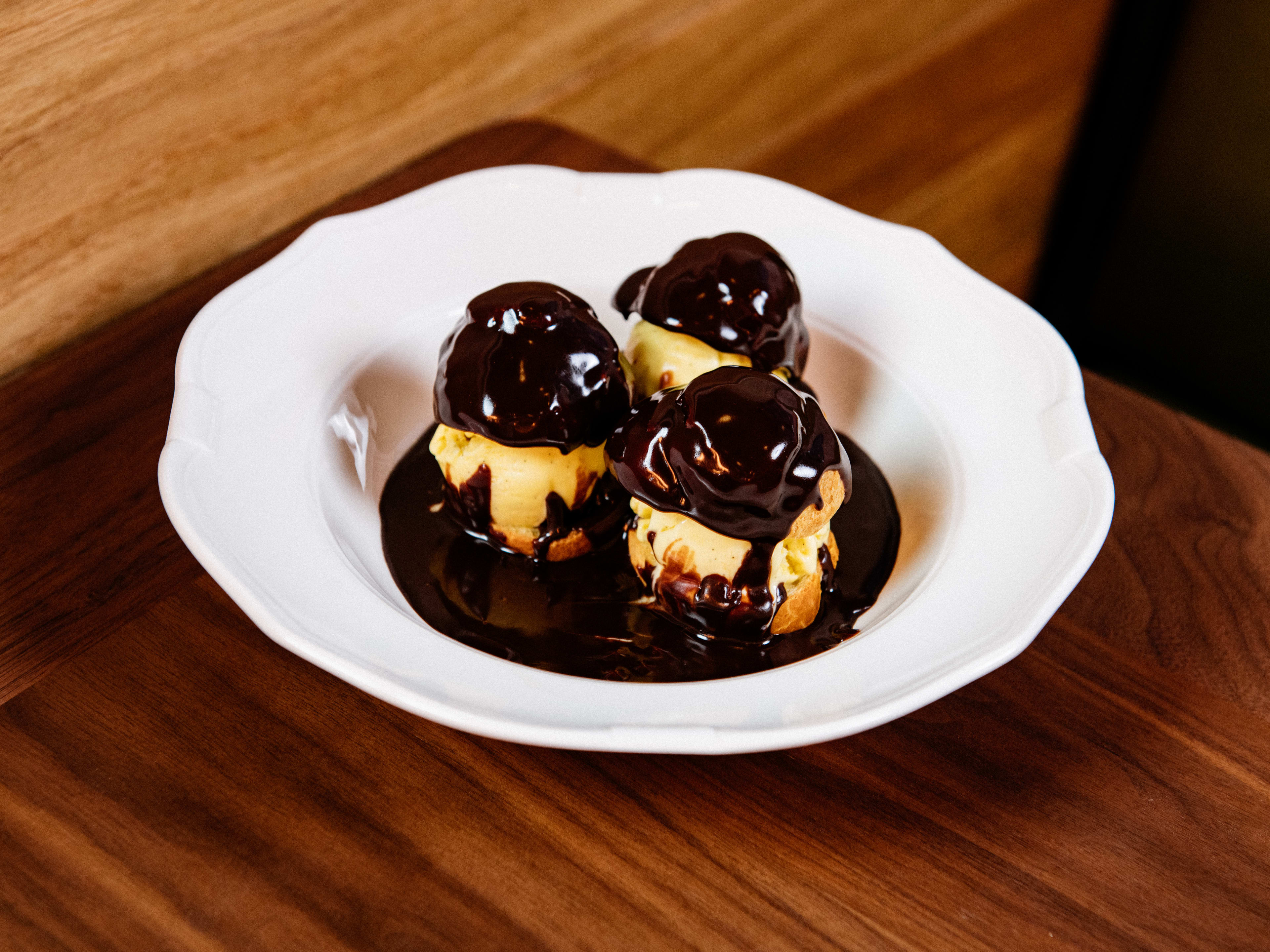 A plate of profiteroles with chocolate sauce on top.