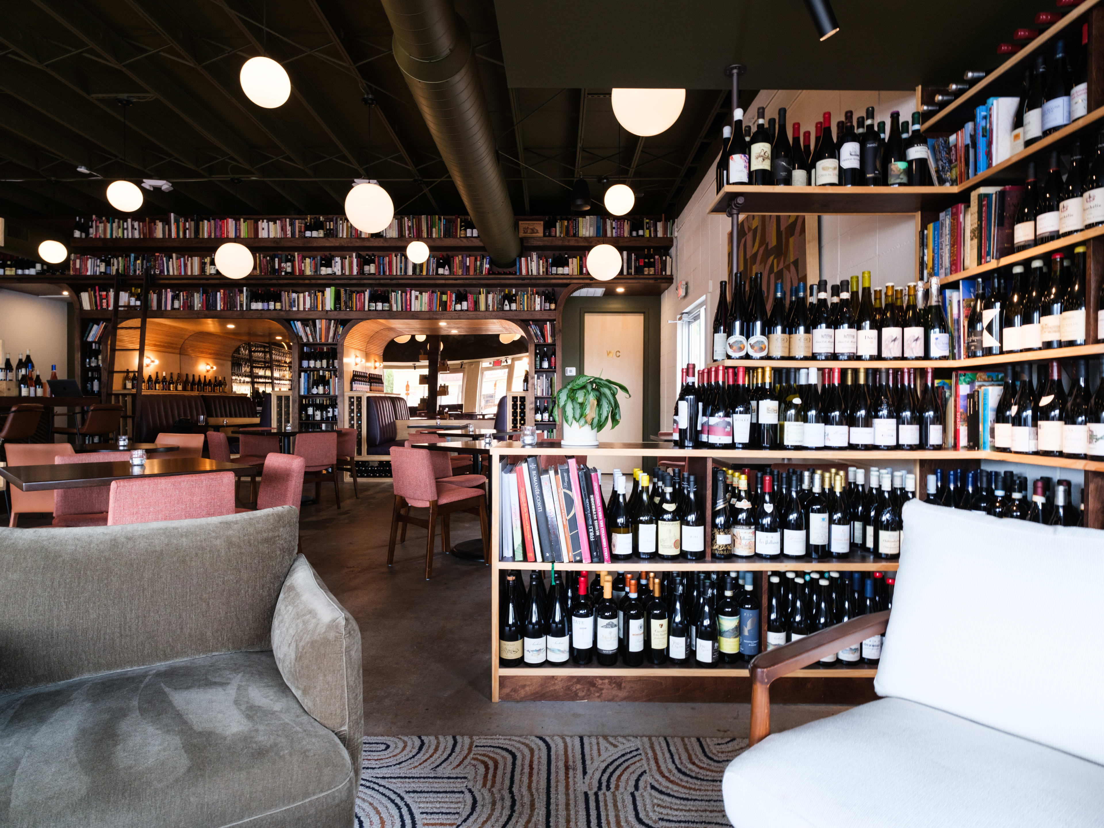 Two lounge chairs in front of sweeping bookshelves filled with wine bottles and books.