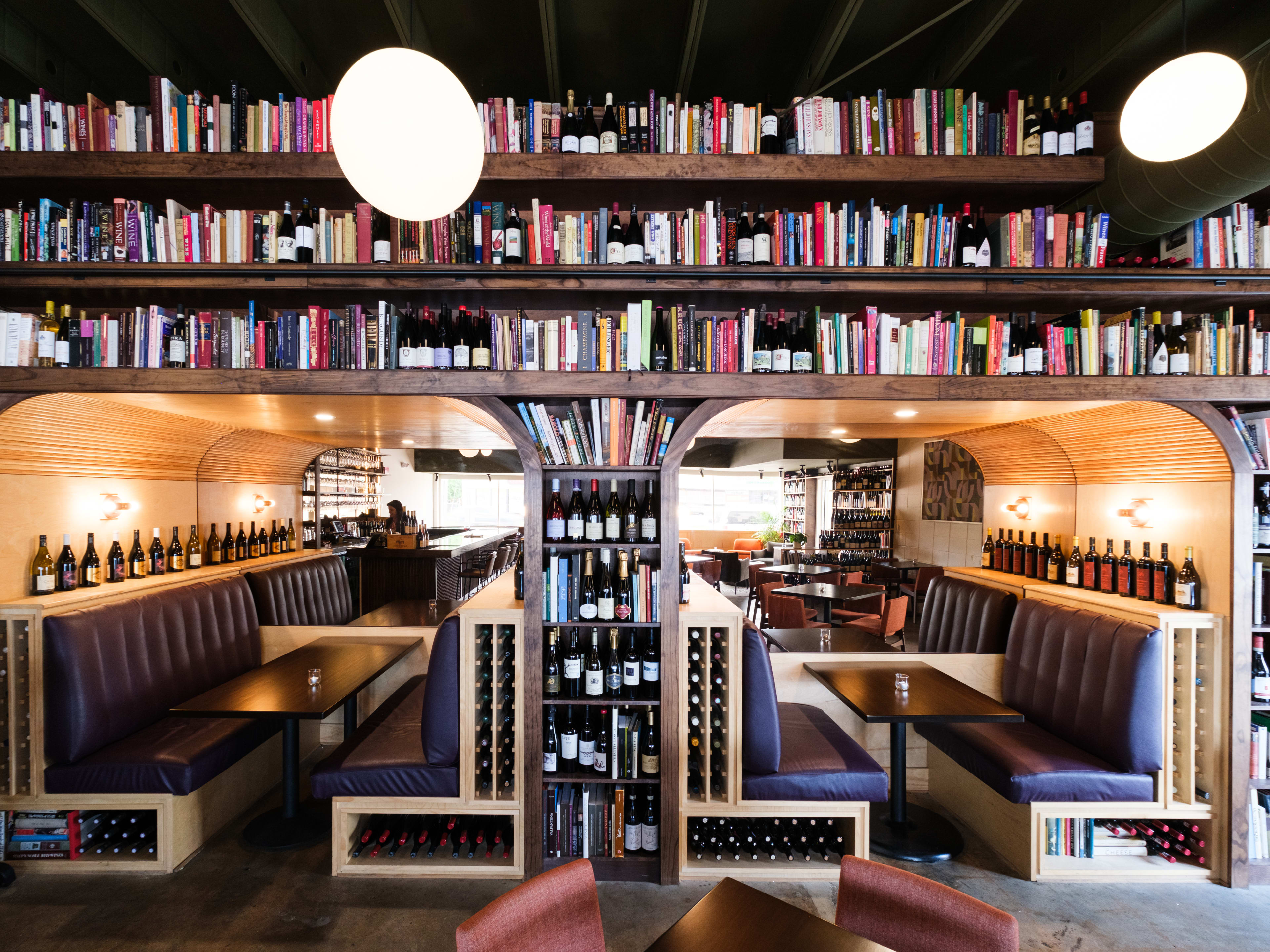 Two booths surrounded by wrap around bookshelves filled with books and wine bottles.