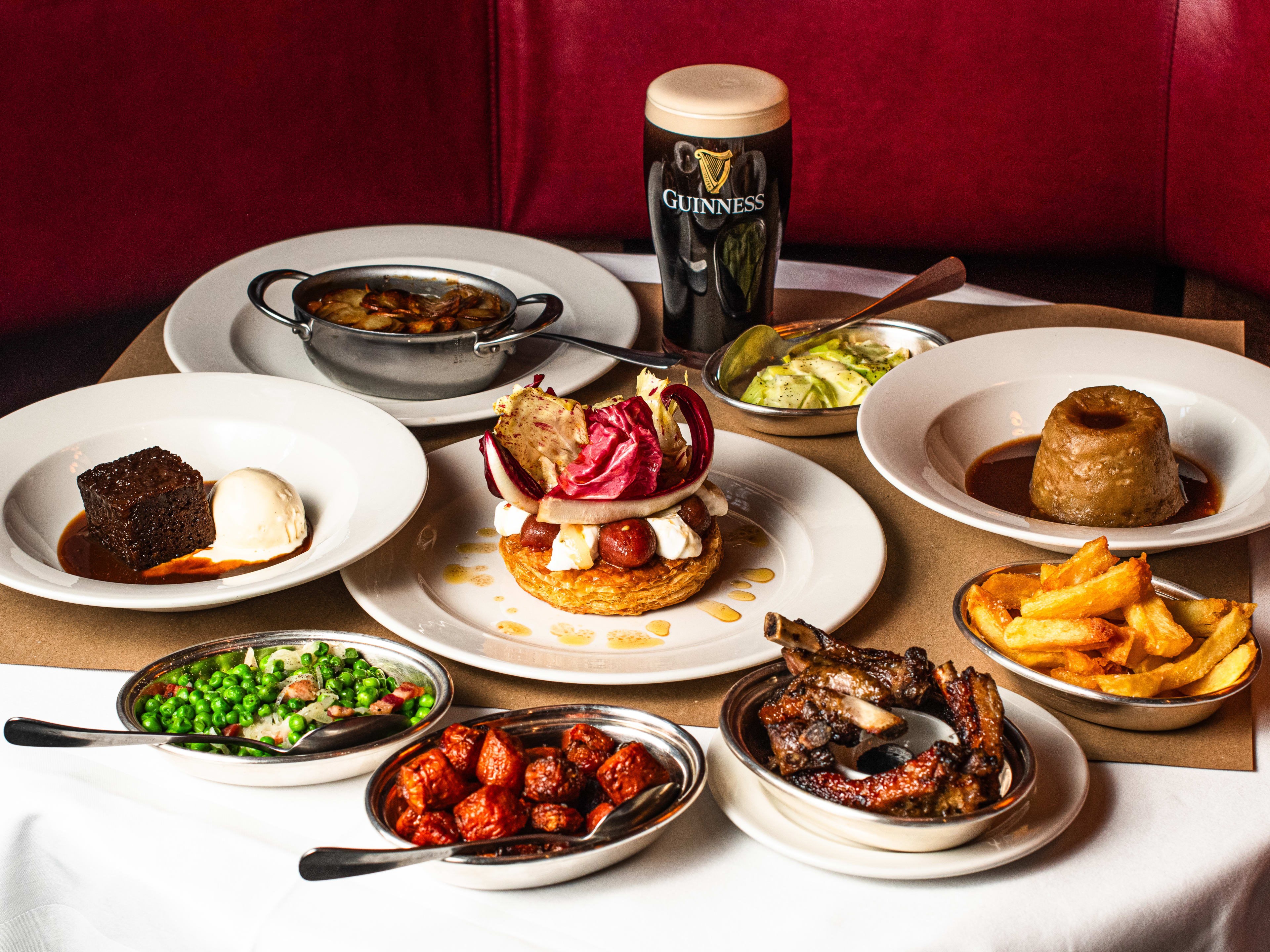 A table at The Devonshire with a pint of Guinness, sticky toffee pudding, and other dishes on it.