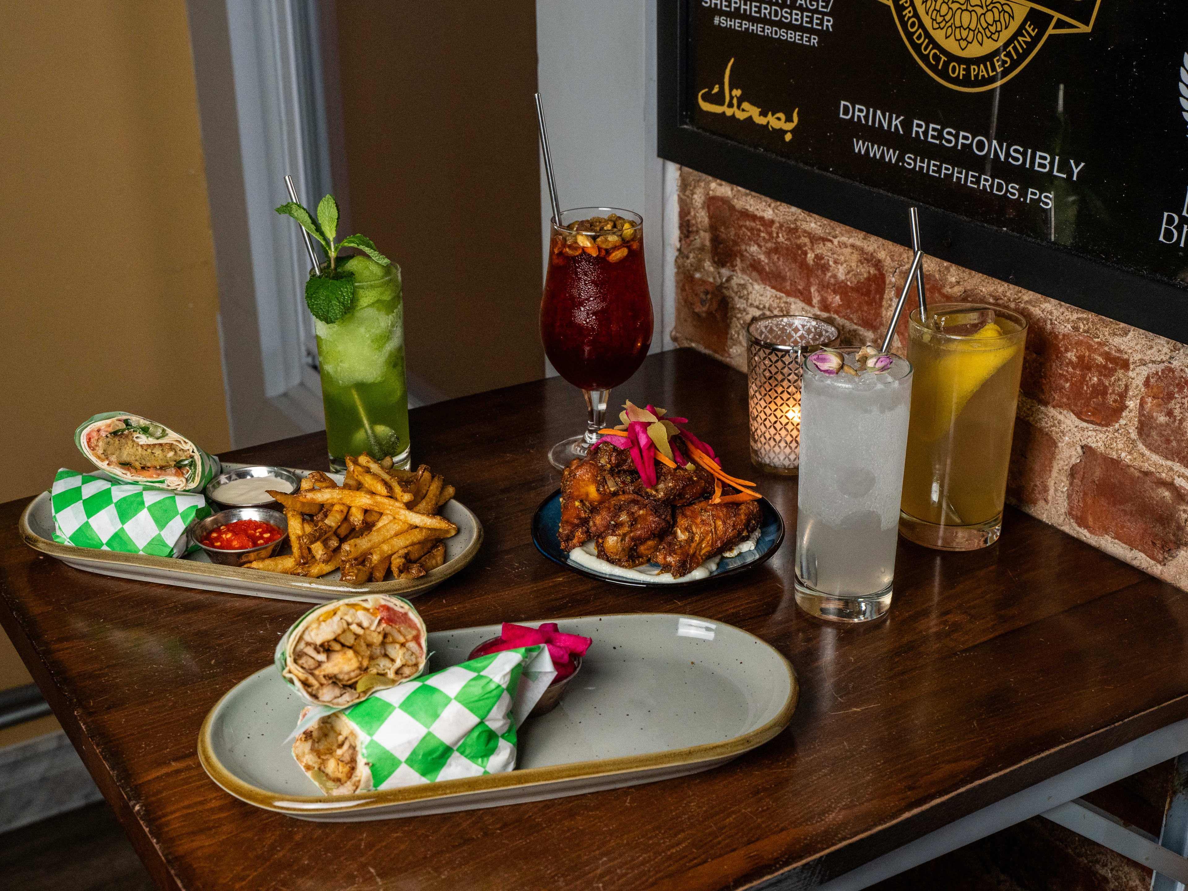 Spread of wraps, wings, fries, and cocktails on wooden table.