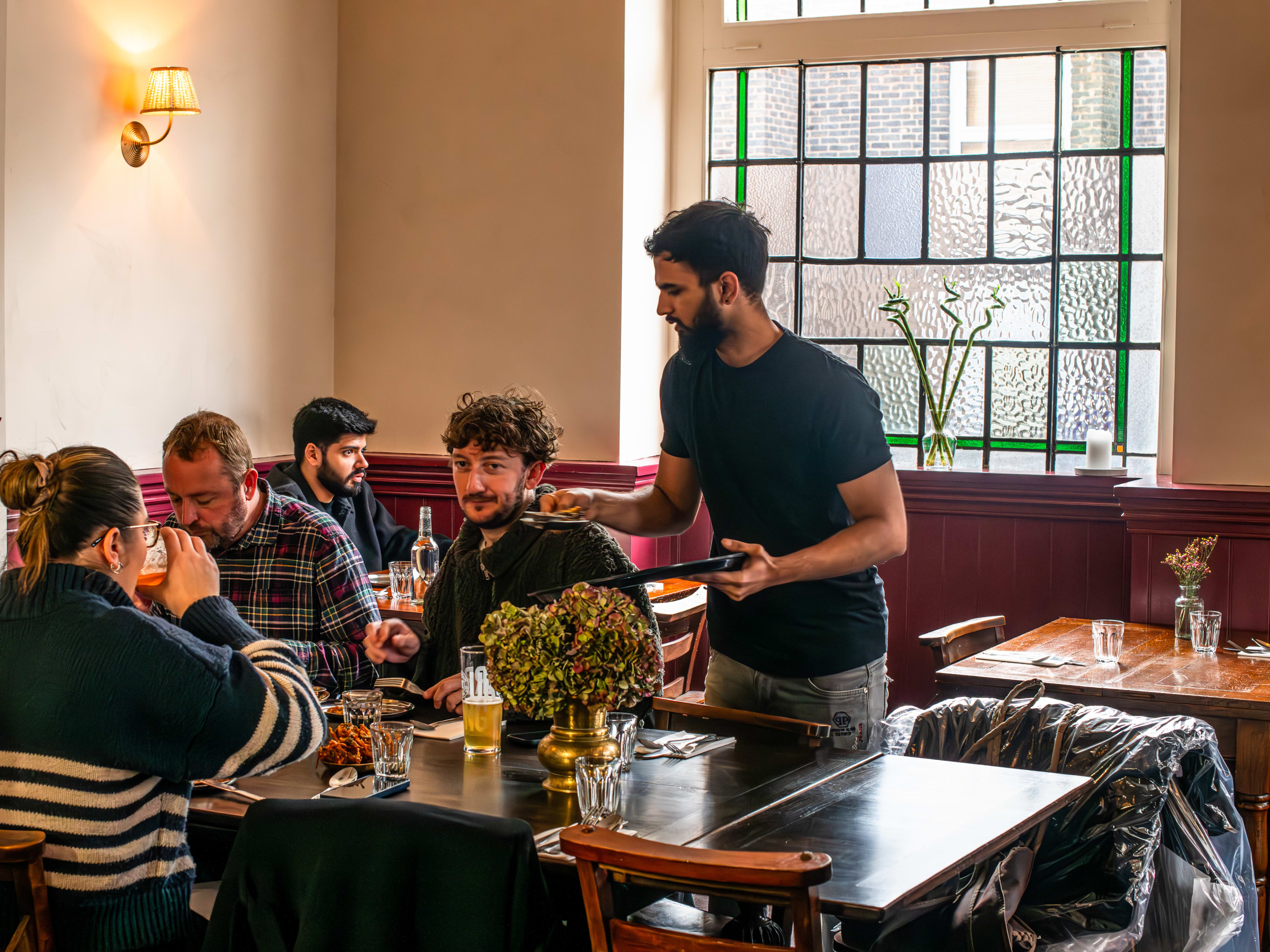 A server hands over a dish to a group of diners at The Tamil Crown.