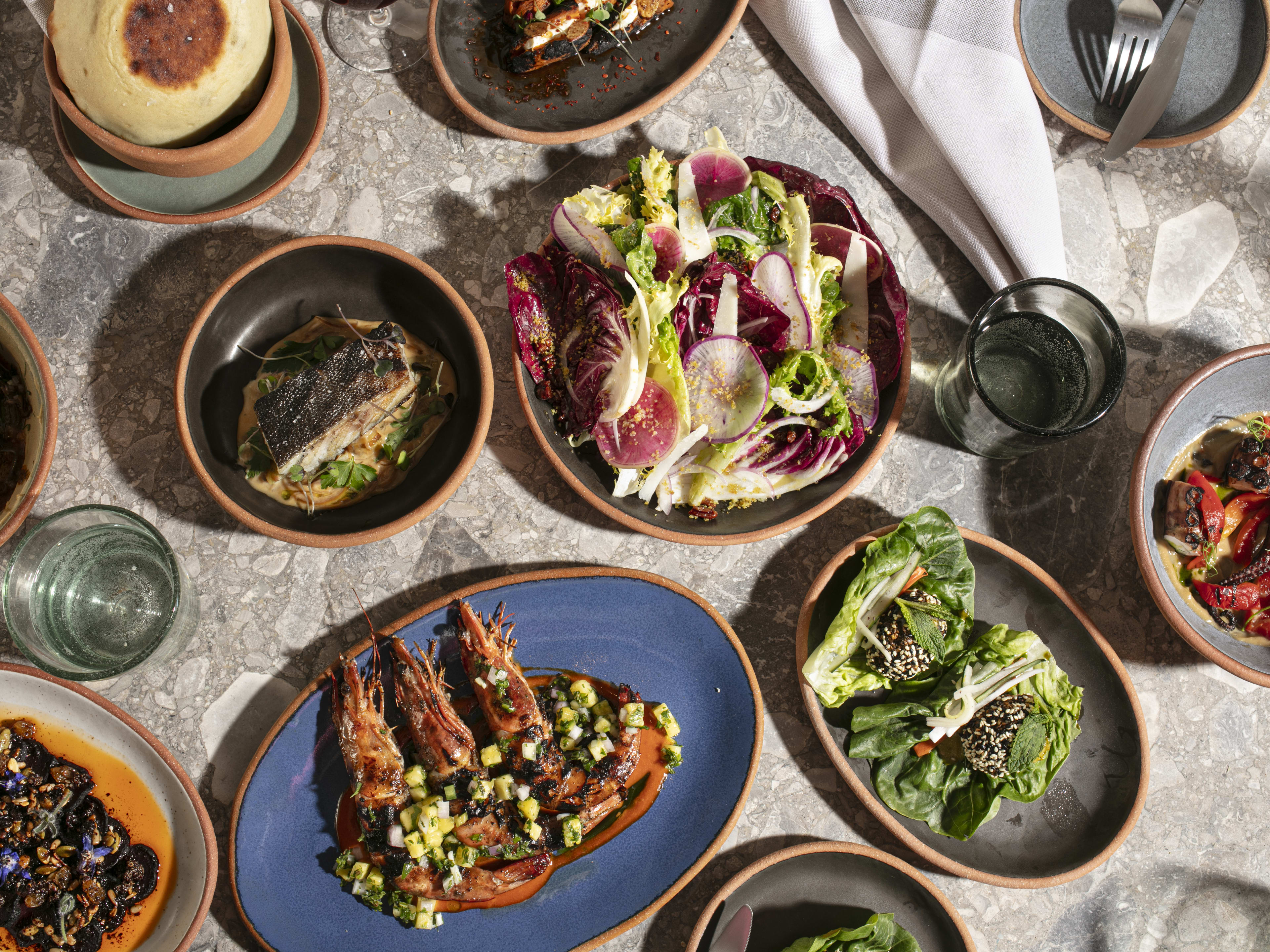 A big spread of food, including salad, grilled shrimp, and octopus, served in colorful ceramic dishes.