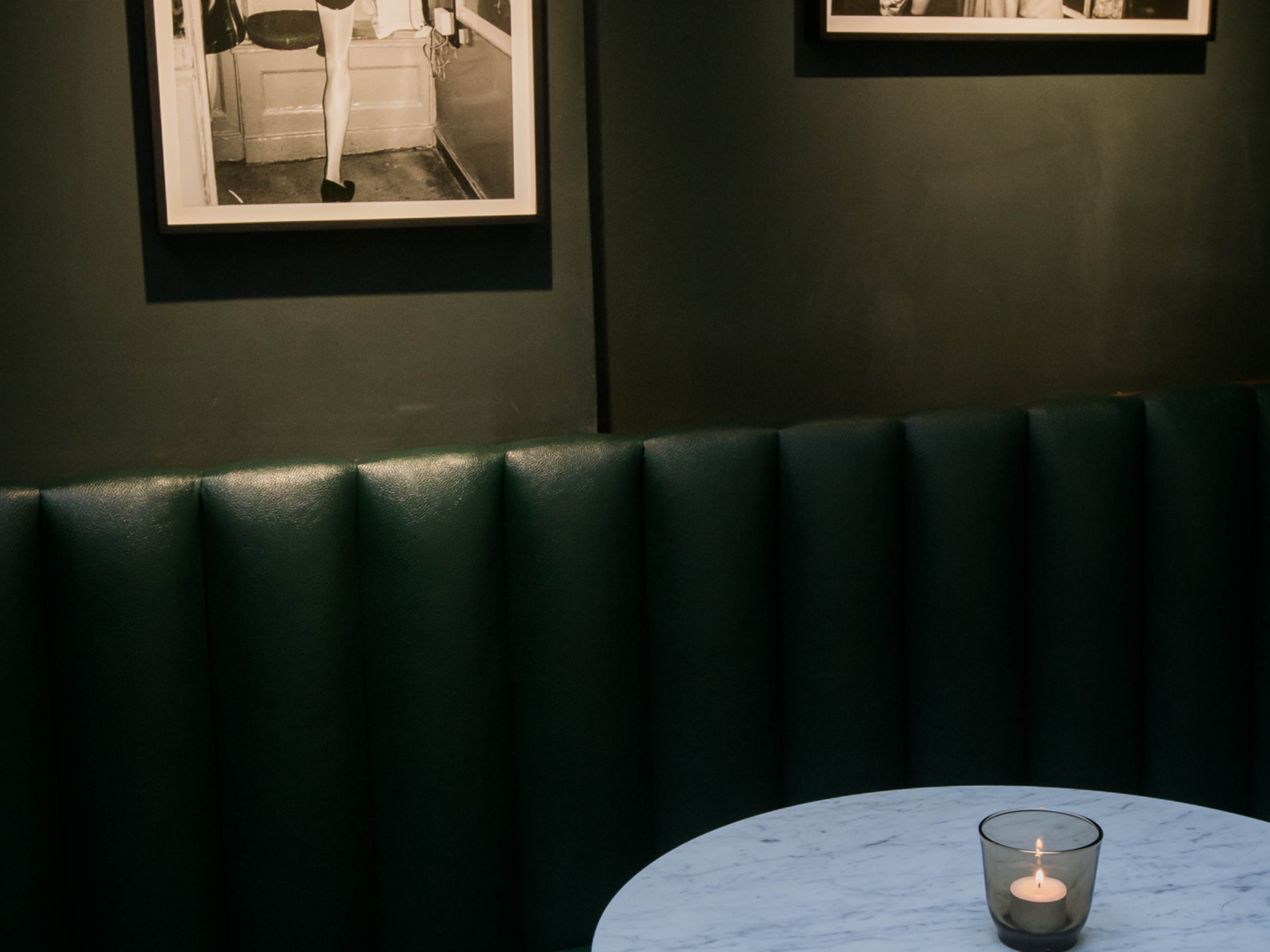 A moody green booth, with a marble-look table with a flickering candle.