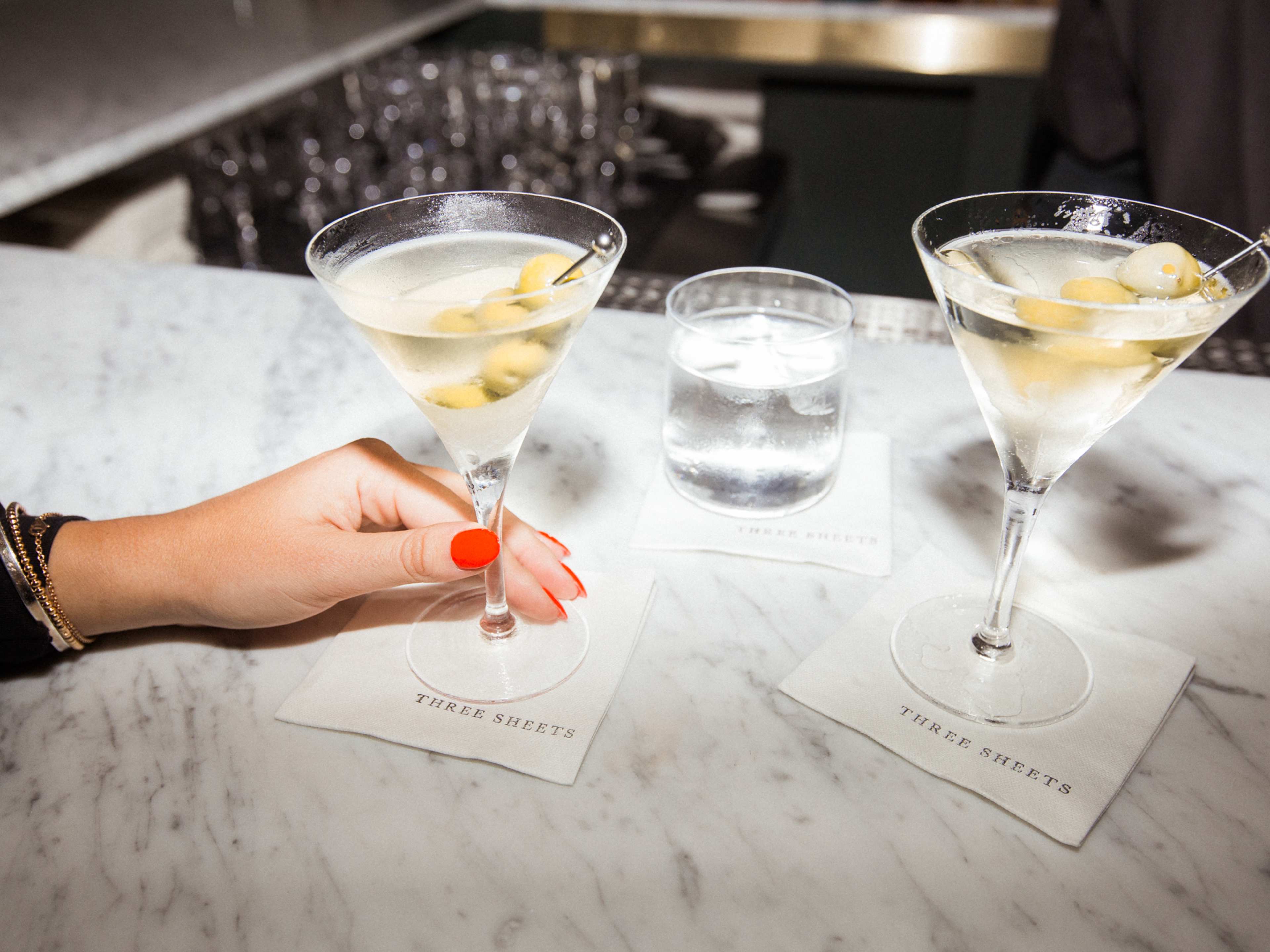 Two dirty martinis on a marble-look bar, and a hand holding one of them.