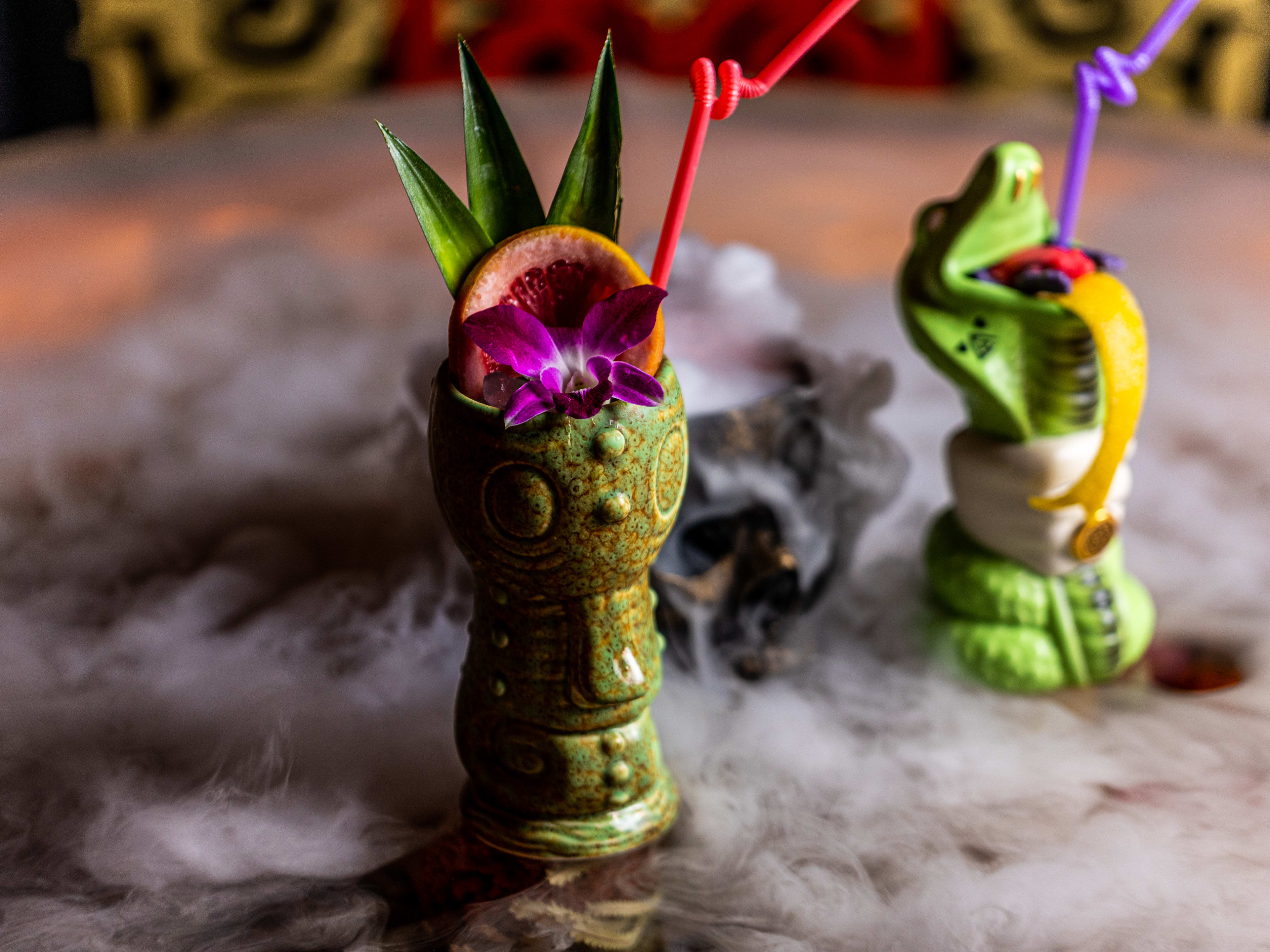 The Cobra Kai and Forbidden Grog cocktails served in themed, ceramic tiki glasses with colorful garnish and bendy straws.