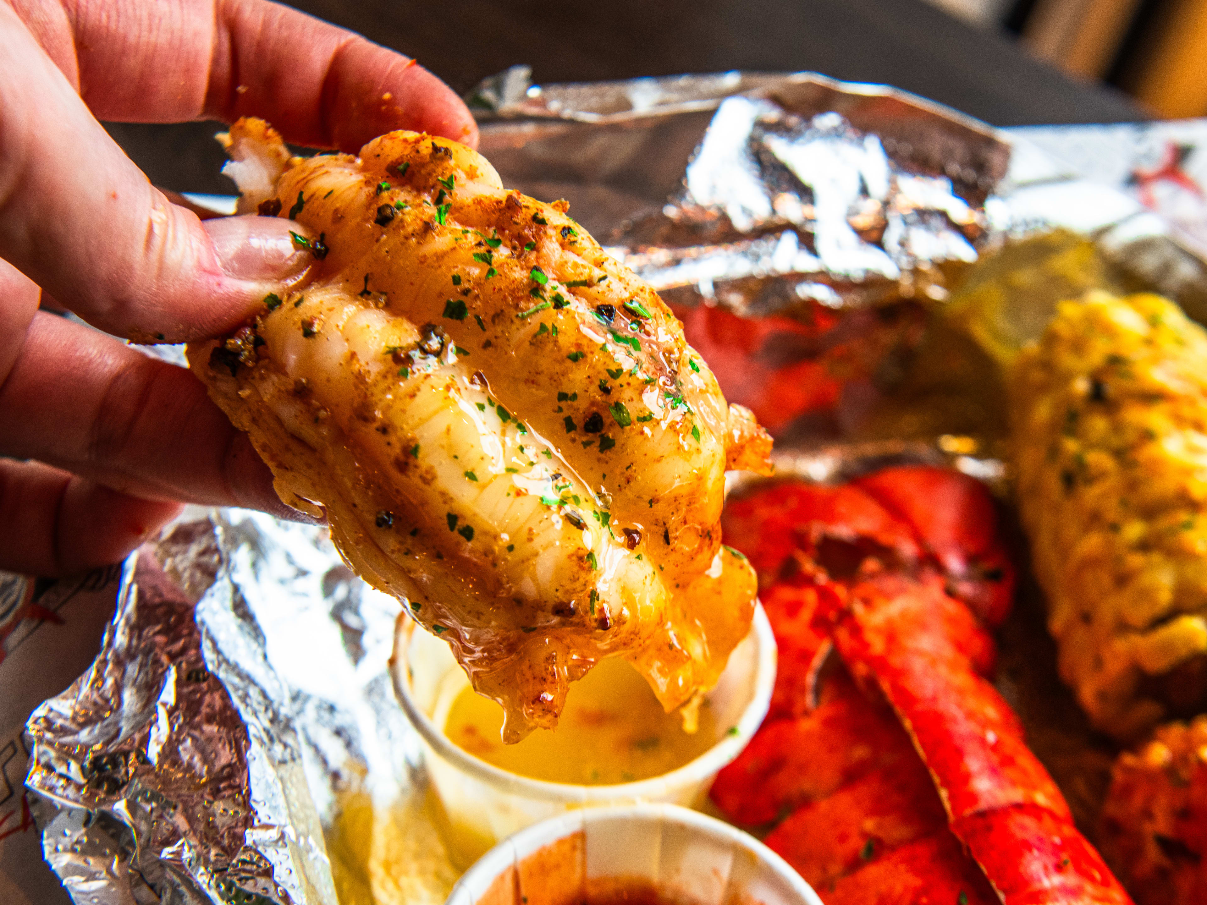 A person dips lobster into butter sauce from Trap Kitchen Camden.