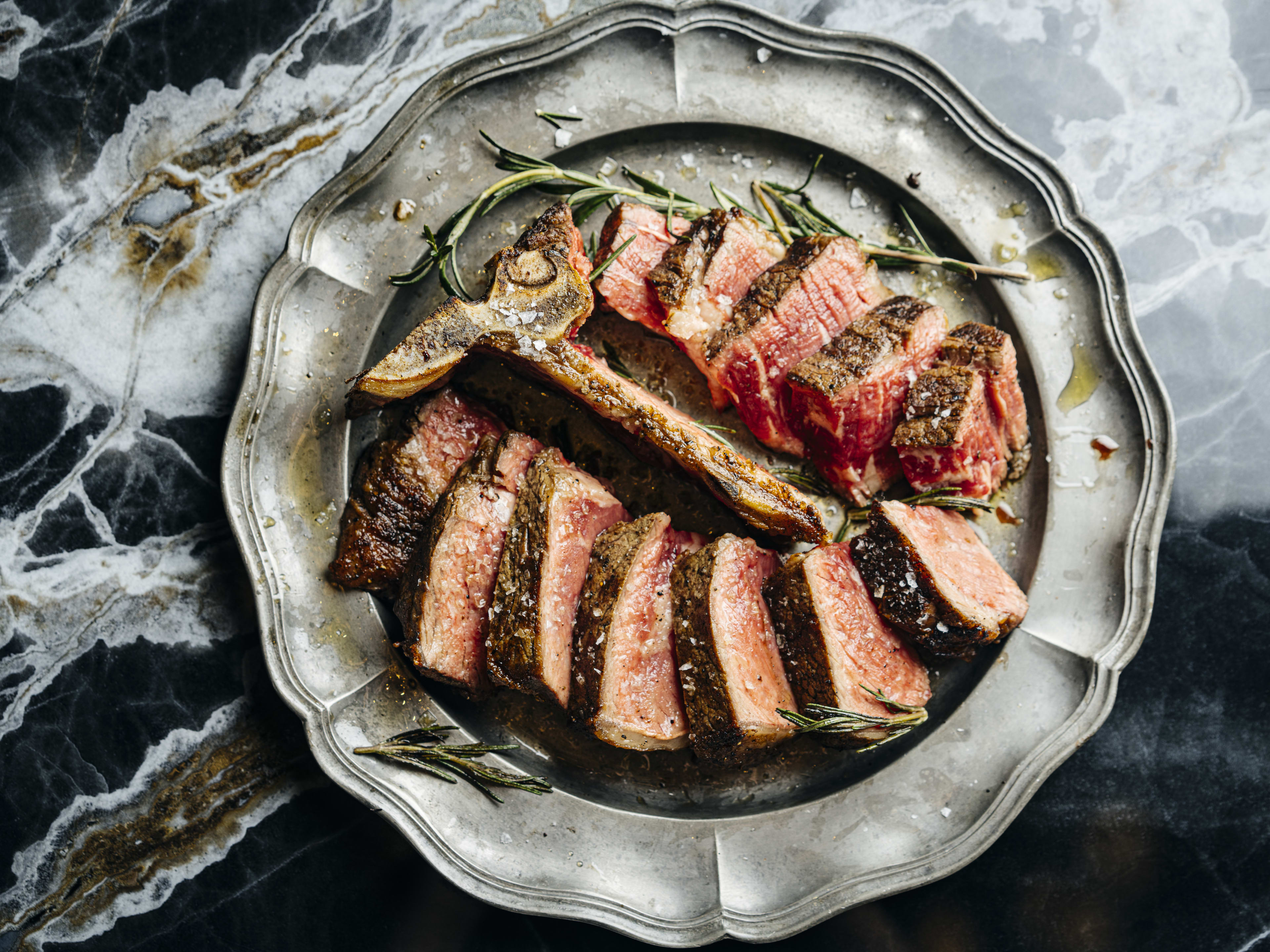 A sliced steak on a metal platter resting on a glossy marble countertop.