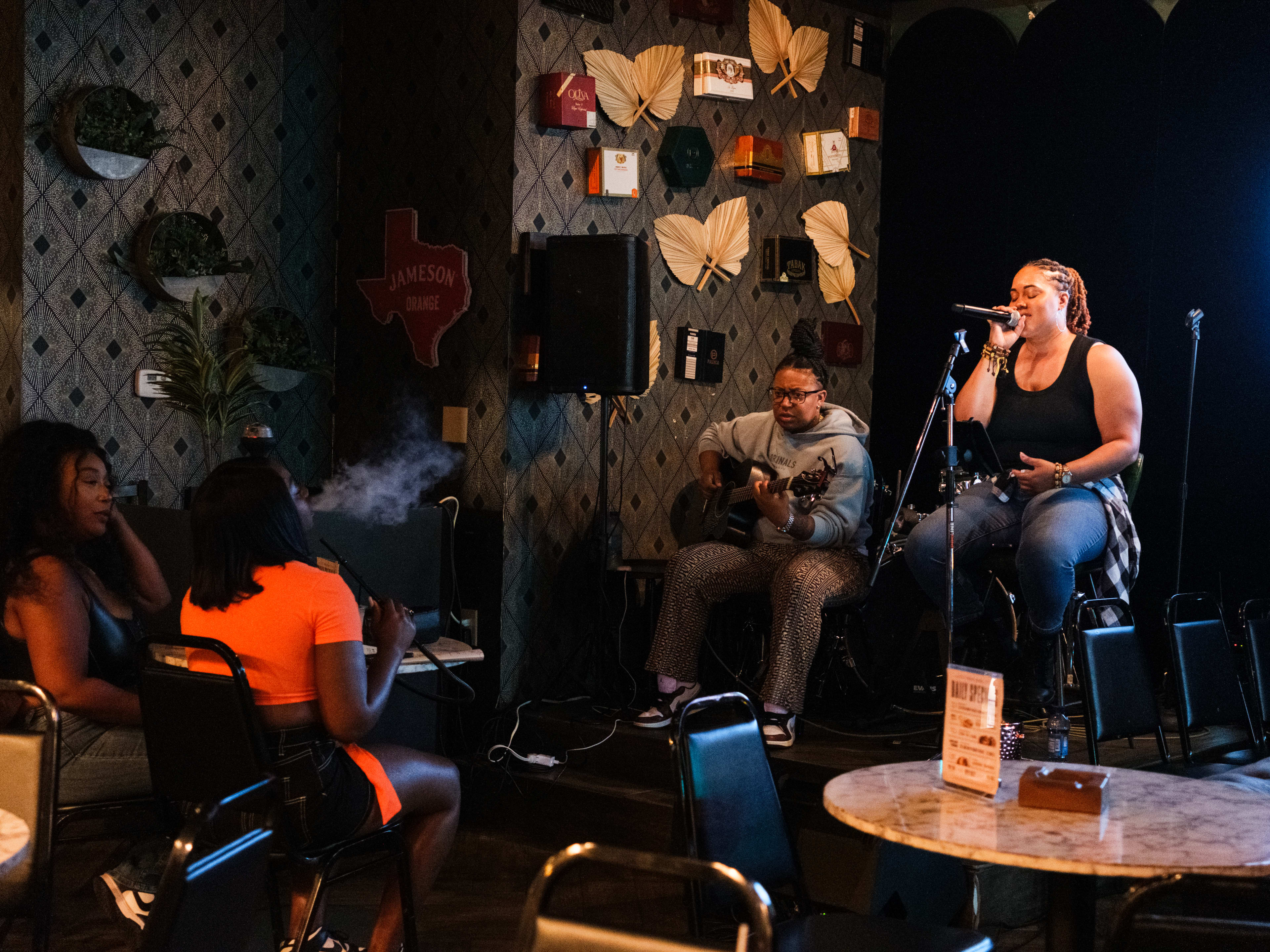 A singer and guitarist perform on stage while two people smoking hookah watch.