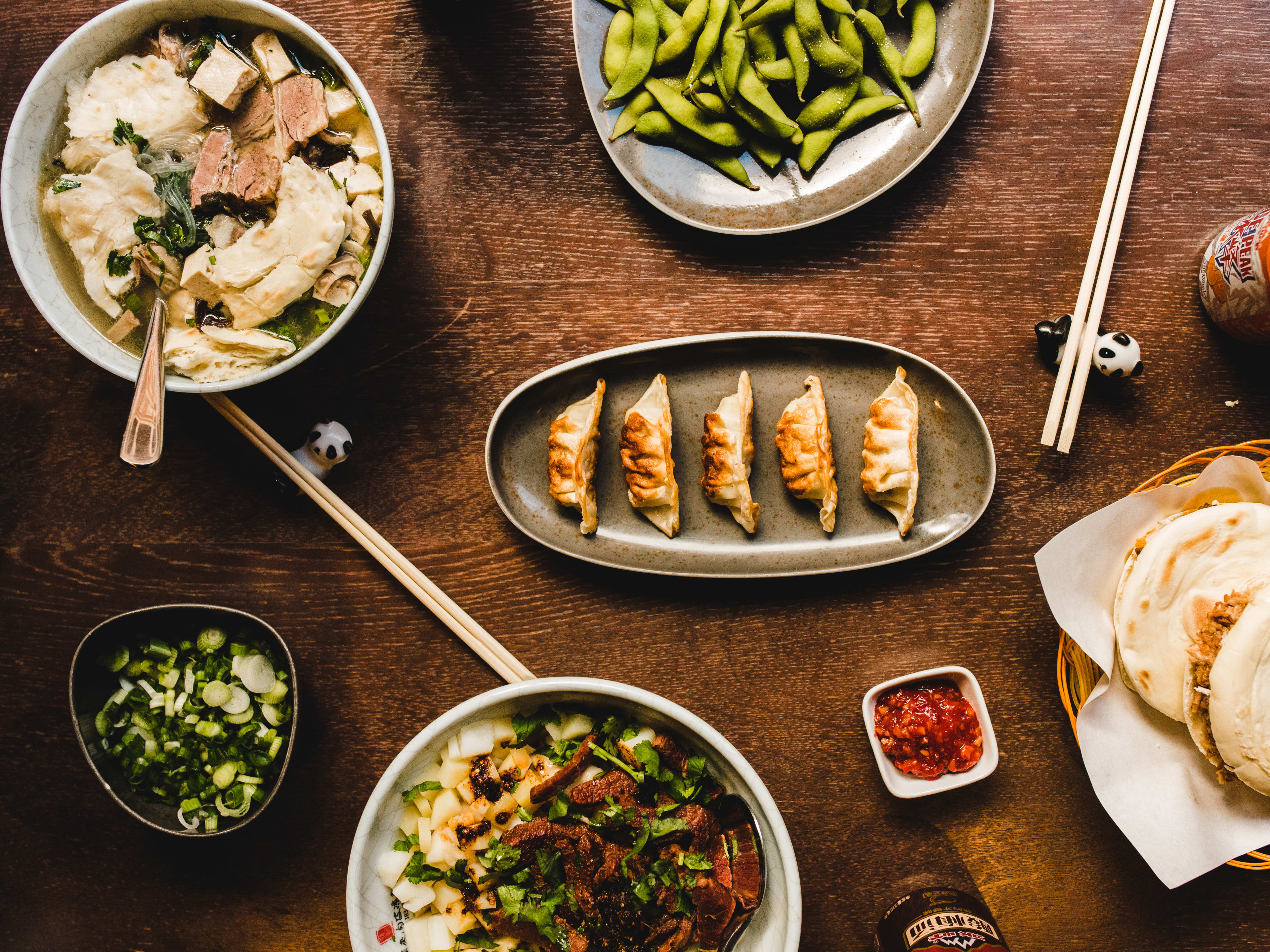 A spread of dishes from Murger Han Mayfair on a wooden table. There are panda chopstick rests as well.