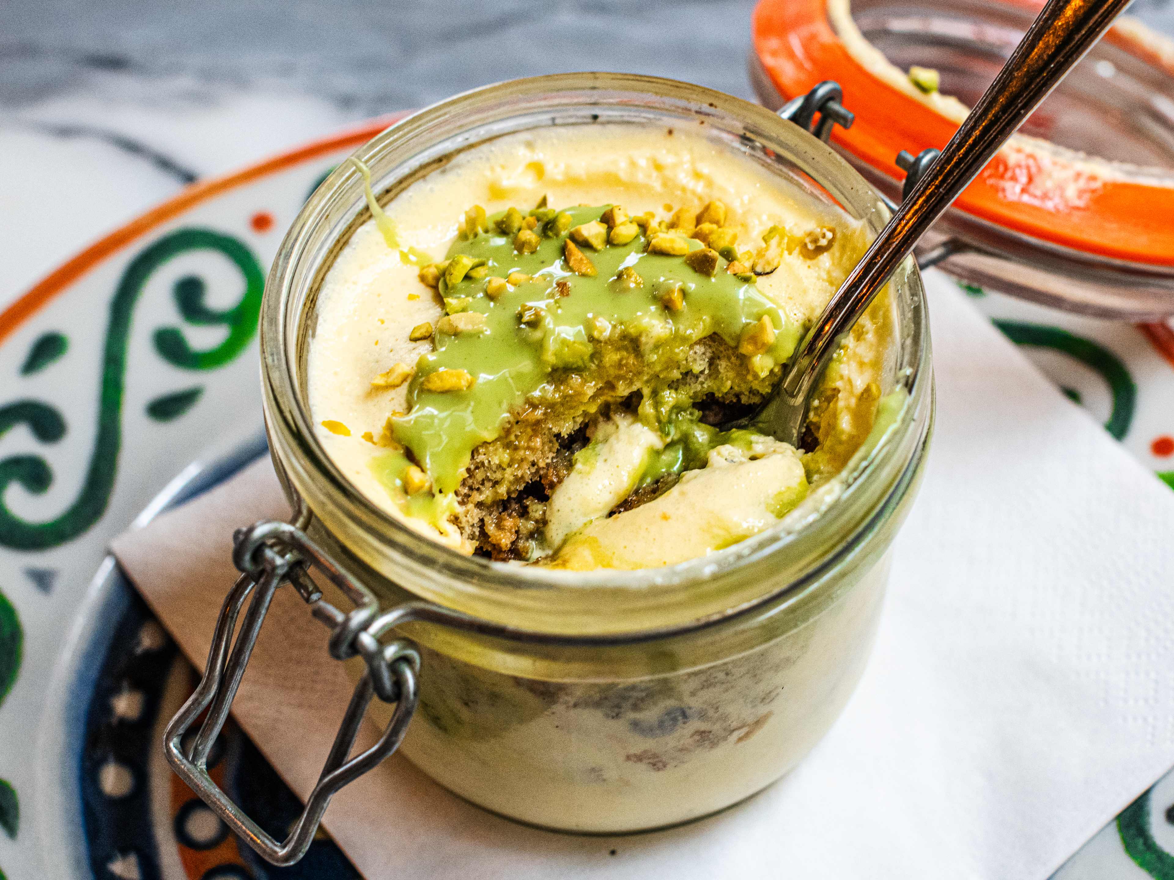 Pistachio tiramisu in a glass ramekin, with a spoon dunked in.