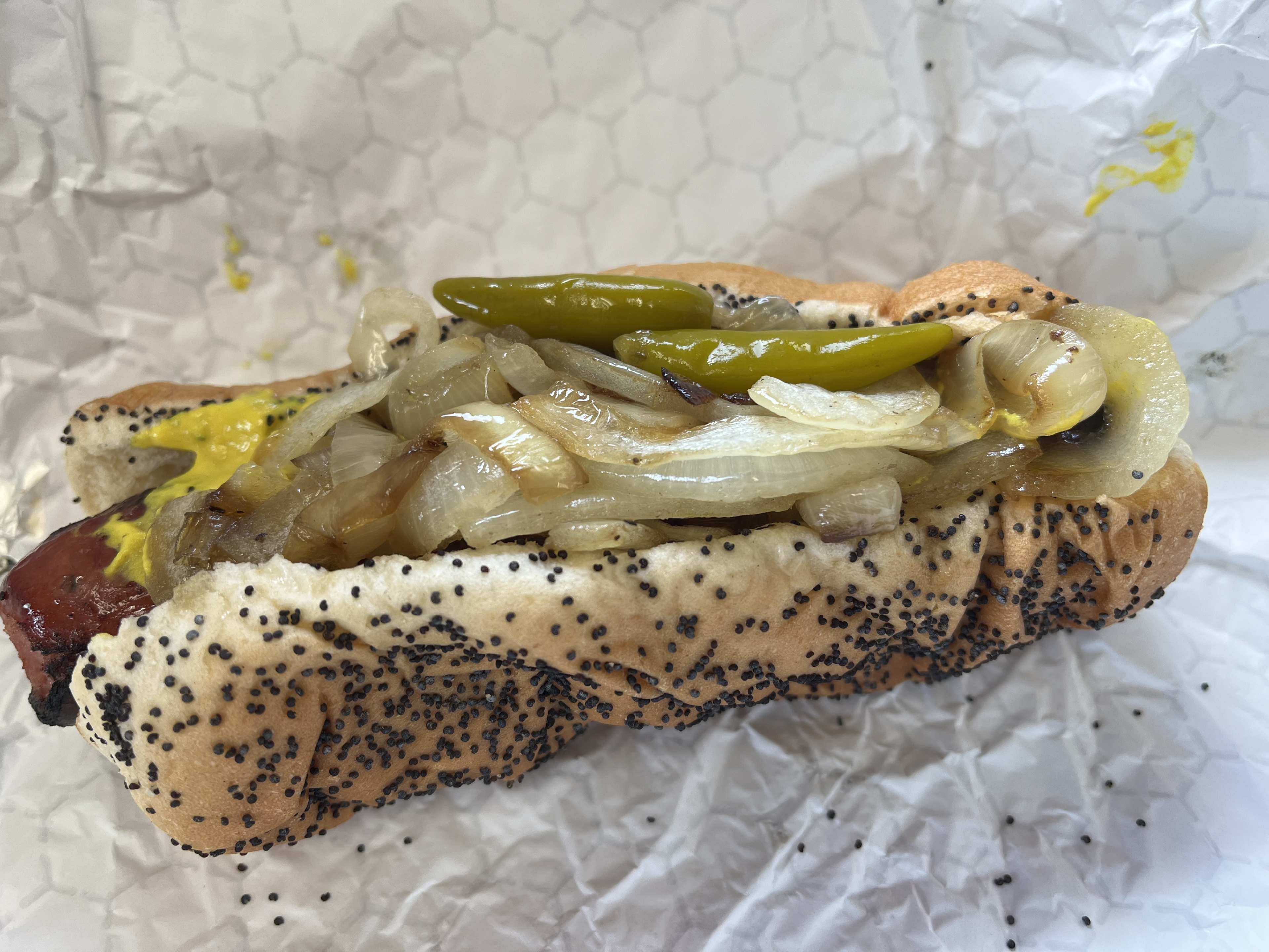 Close-up of a Maxwell polish on a poppy seed bun topped with grilled onions and sport peppers