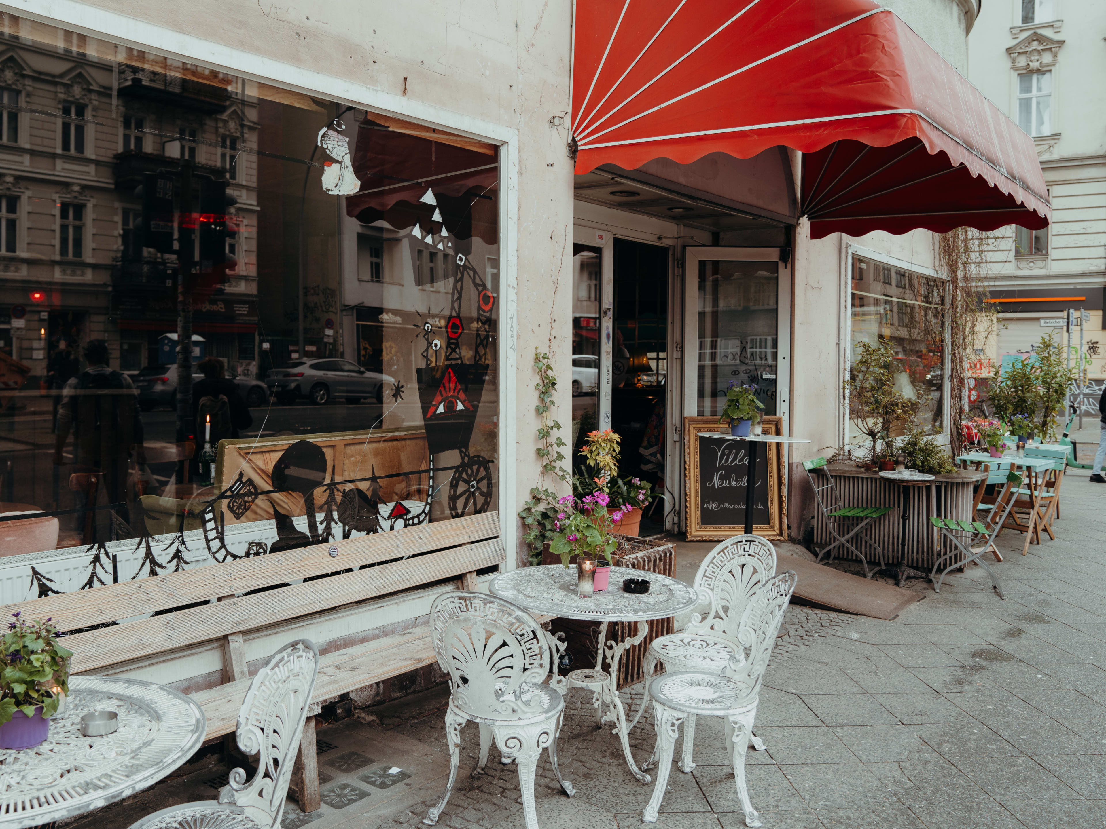 Exterior of Villa Neukolln with red awning and white outdoor tables