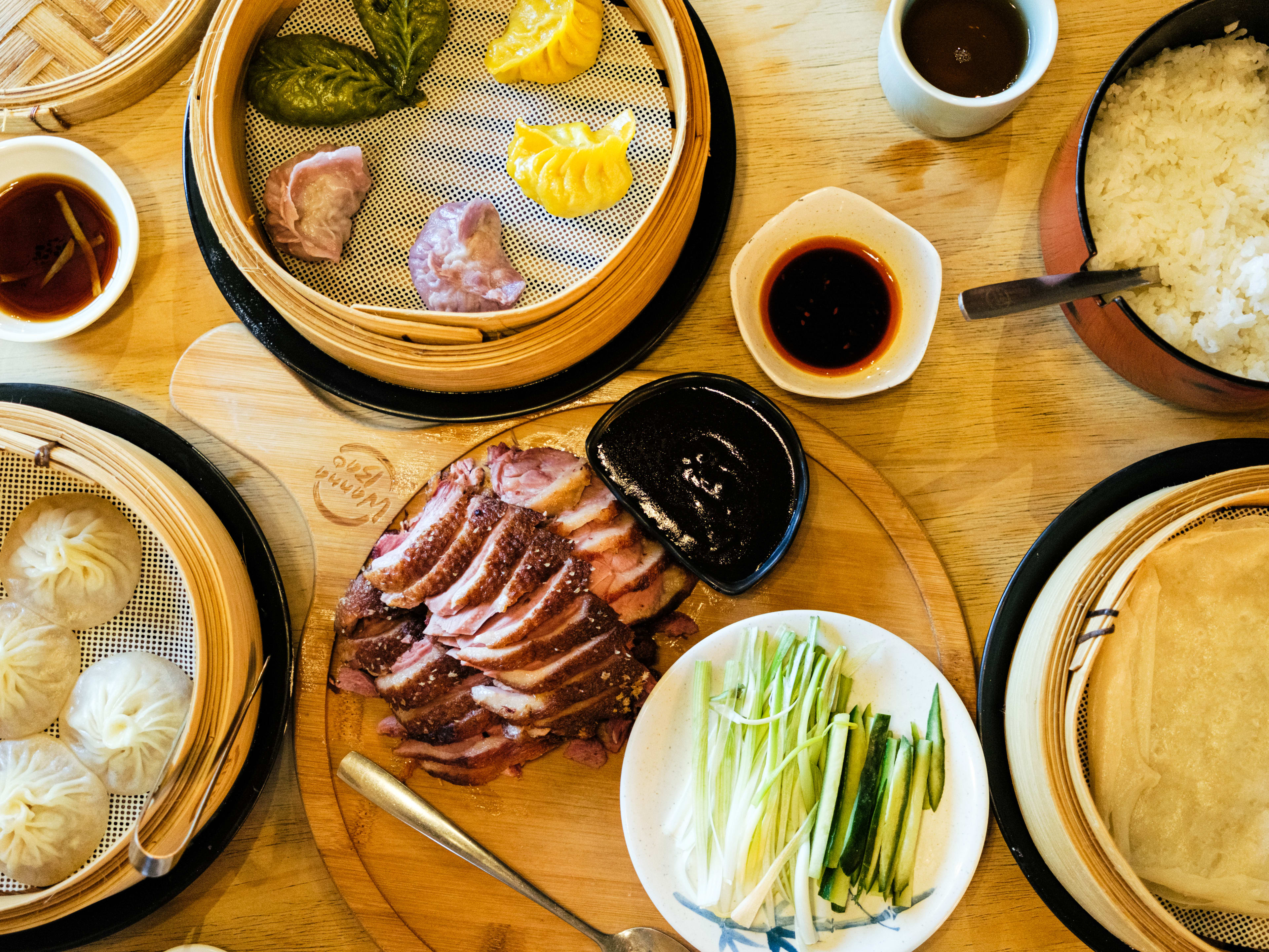 spread of Chinese food with colorful dumpkings, soup dumplings, and sliced duck breast