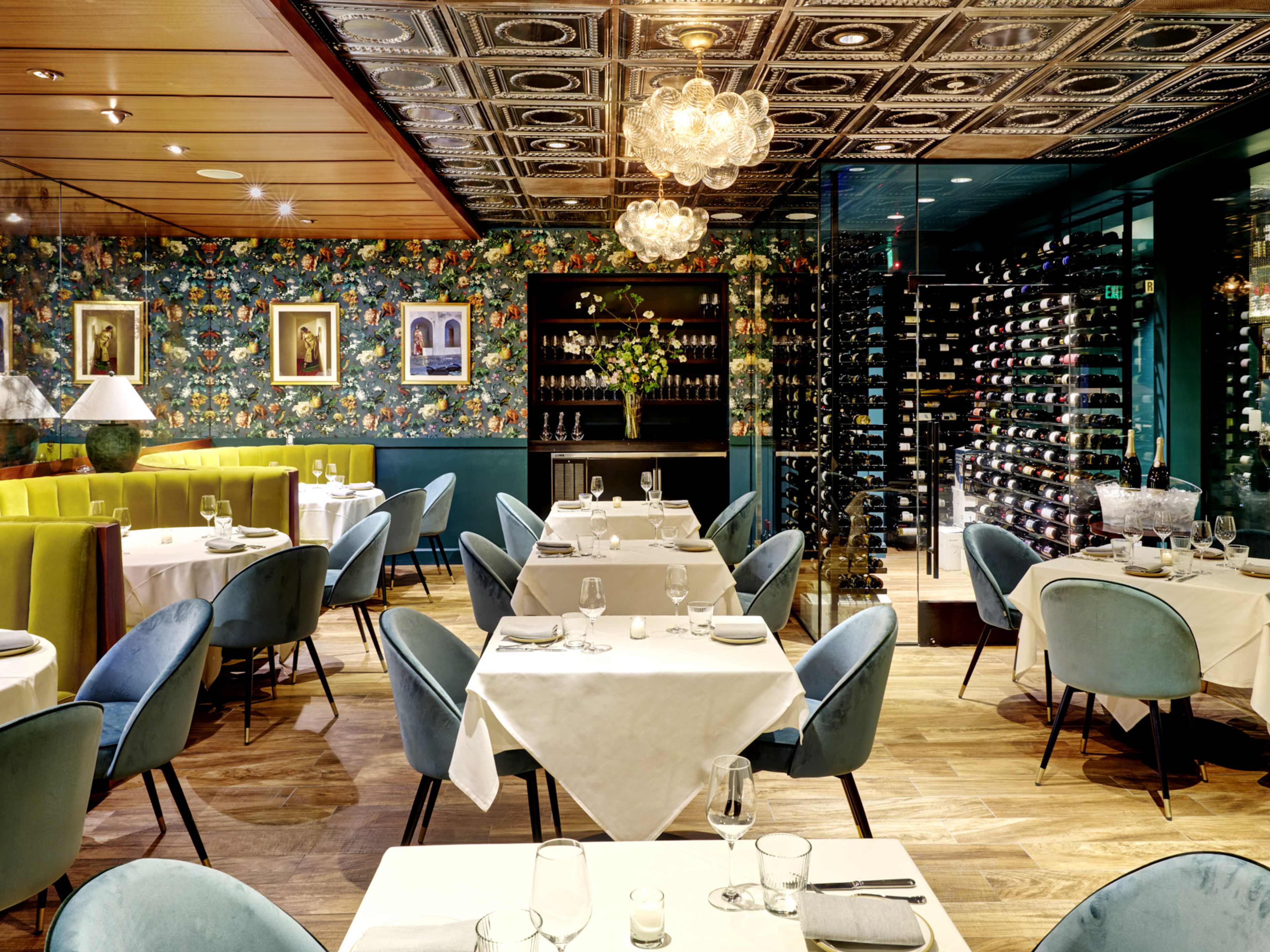 interior of restaurant with velvet booths and chairs, floral wallpaper, and ornate lighting