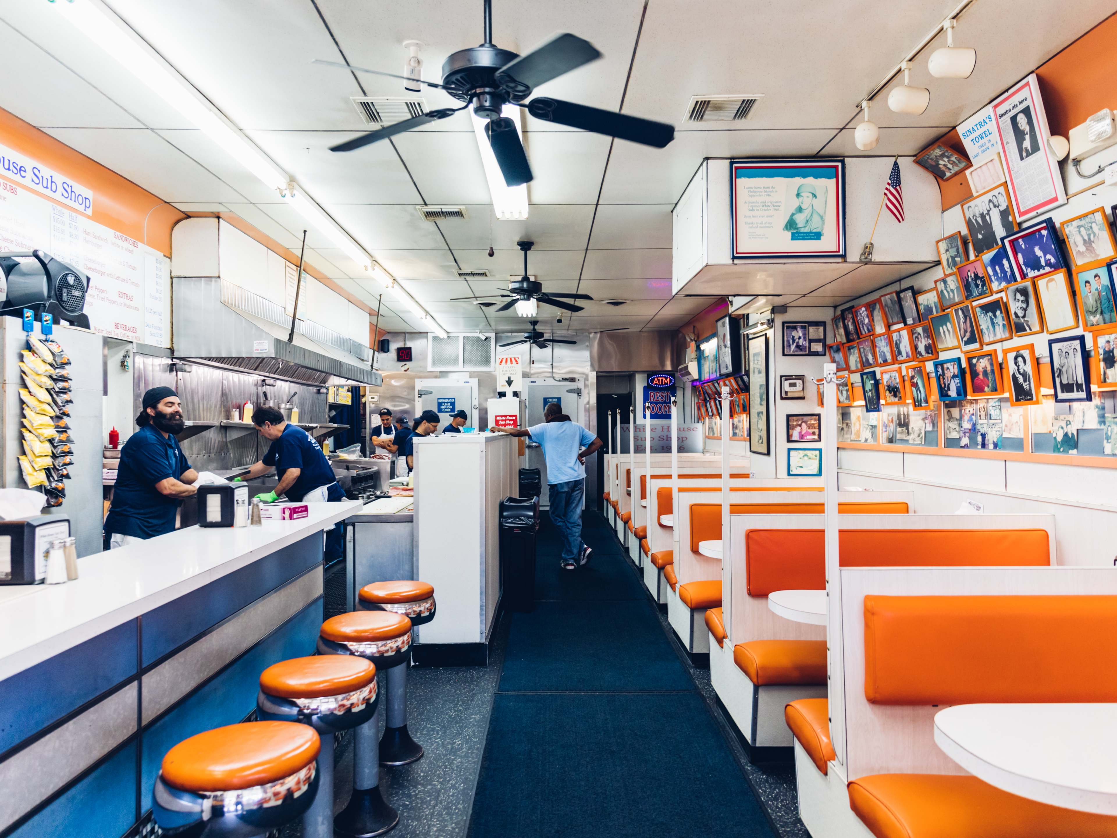 The white and orange interior of a sandwich shop with orange booths and diner stools.