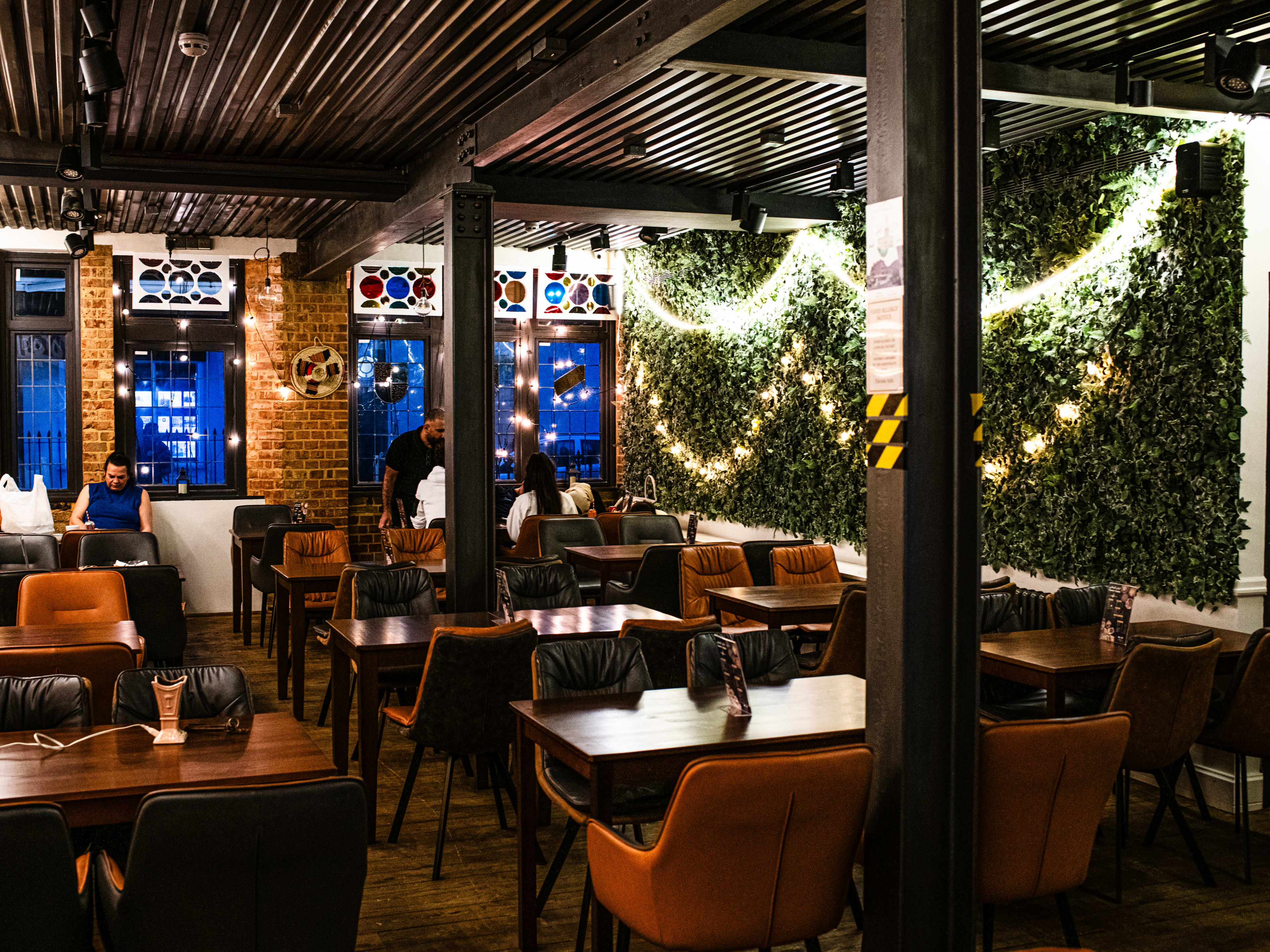 Restaurant interior with brown seats and a foliage wall with hanging lights.