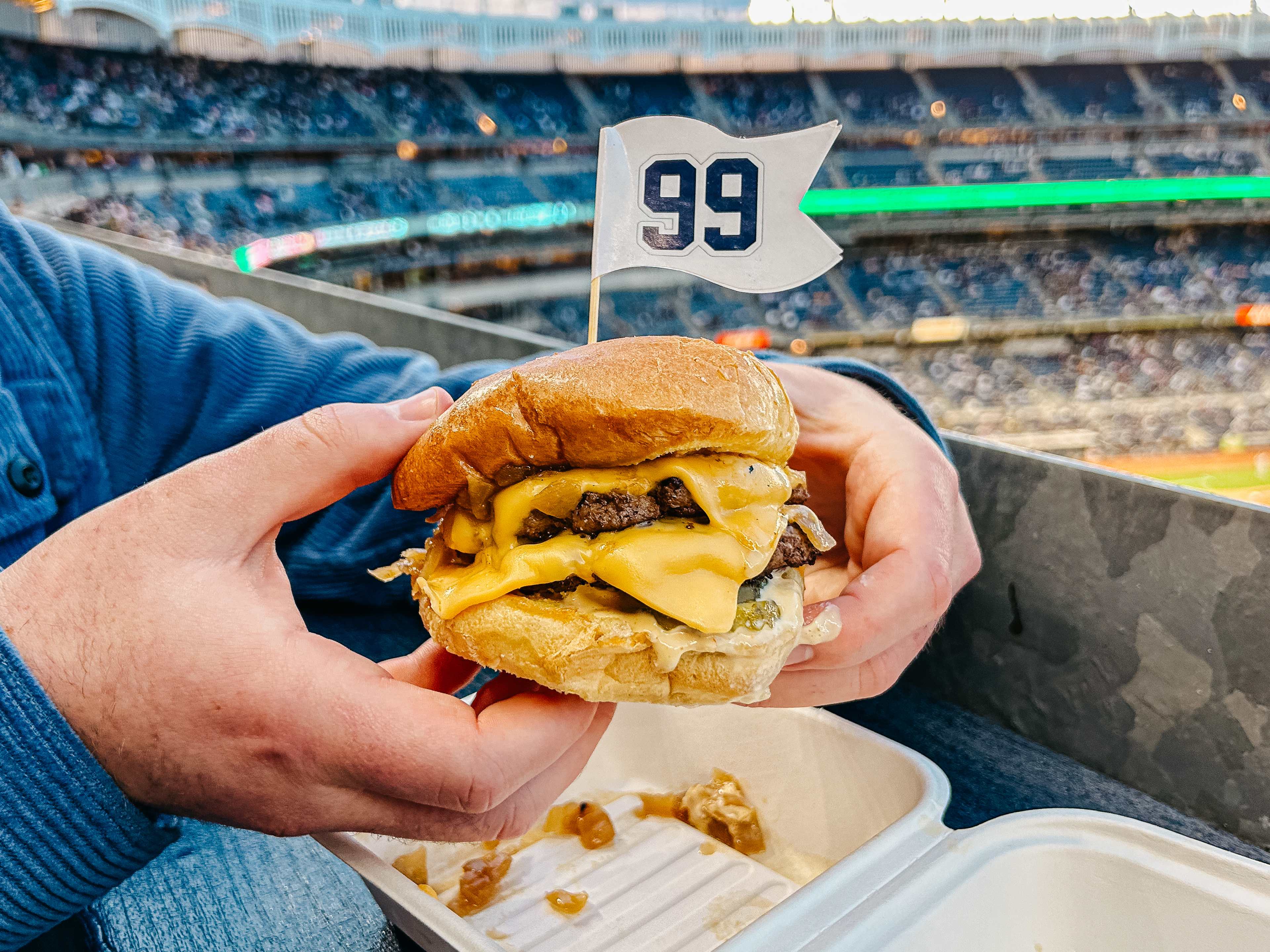 a cheeseburger with a toothpick in it with yankee stadium in the background