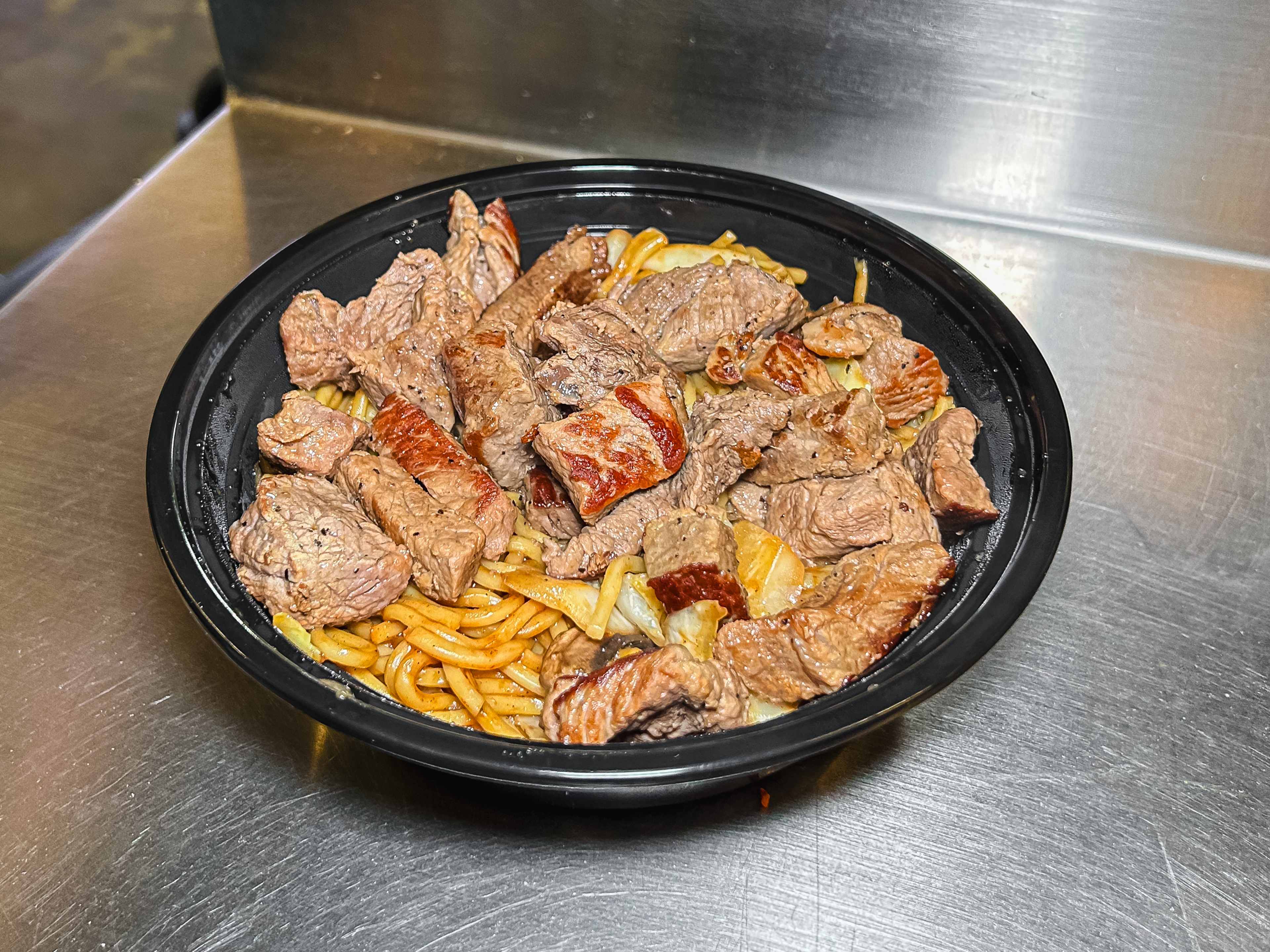 a bowl of stir fried noodles with steak