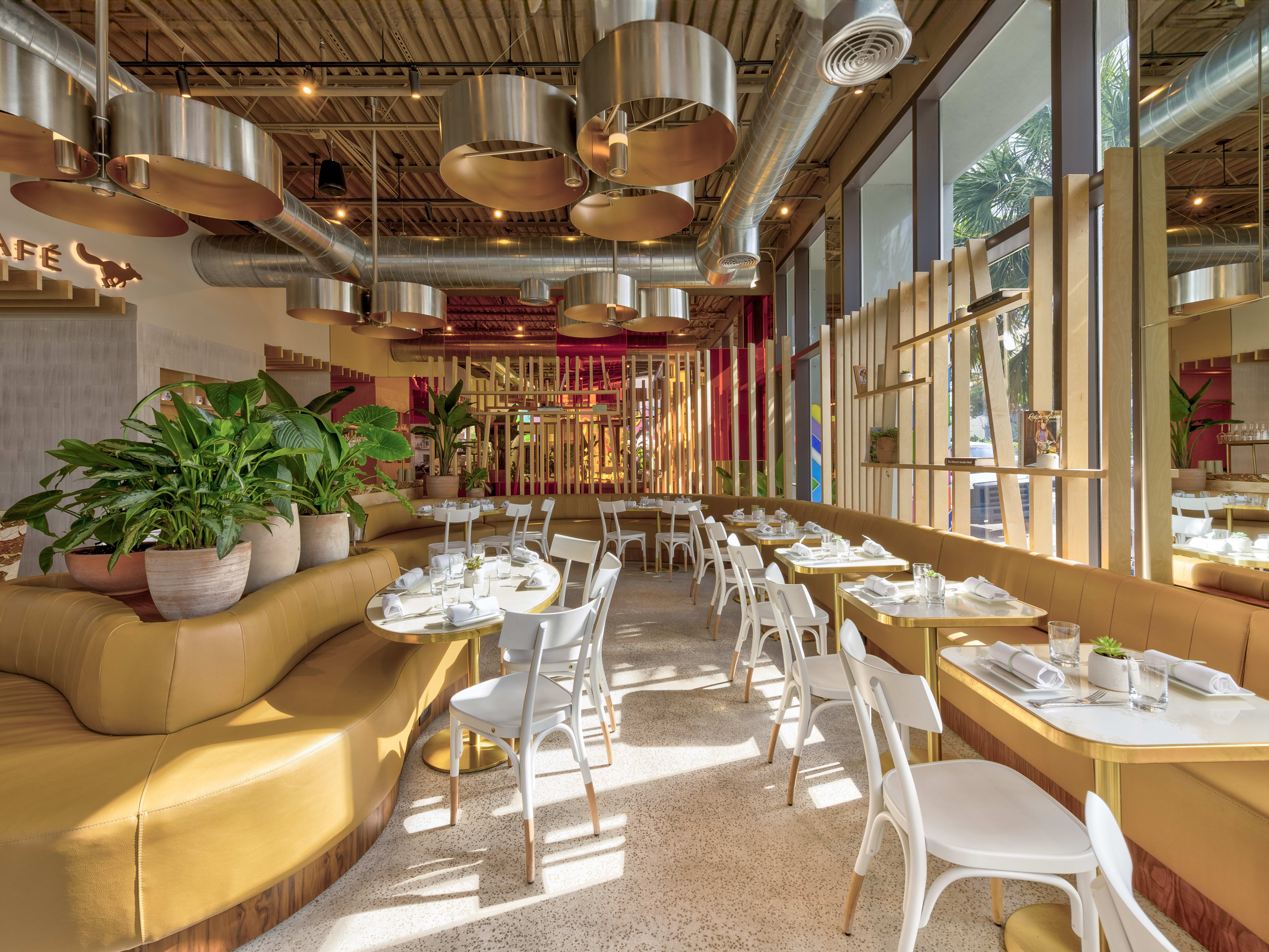 A bright cafe with leather tan booths and white chairs.