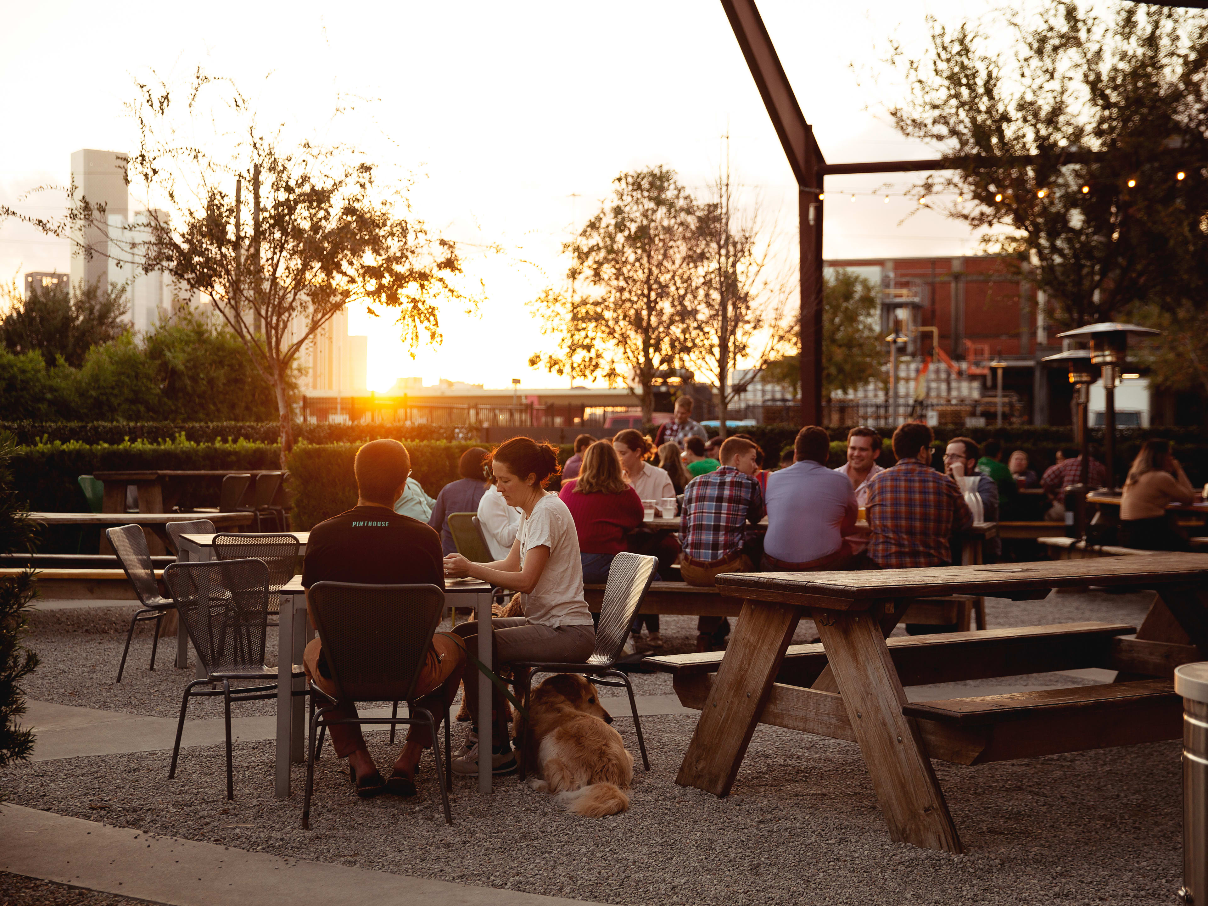 People sit on the patio at Saint Arnold Brewing Company as the sun sets.