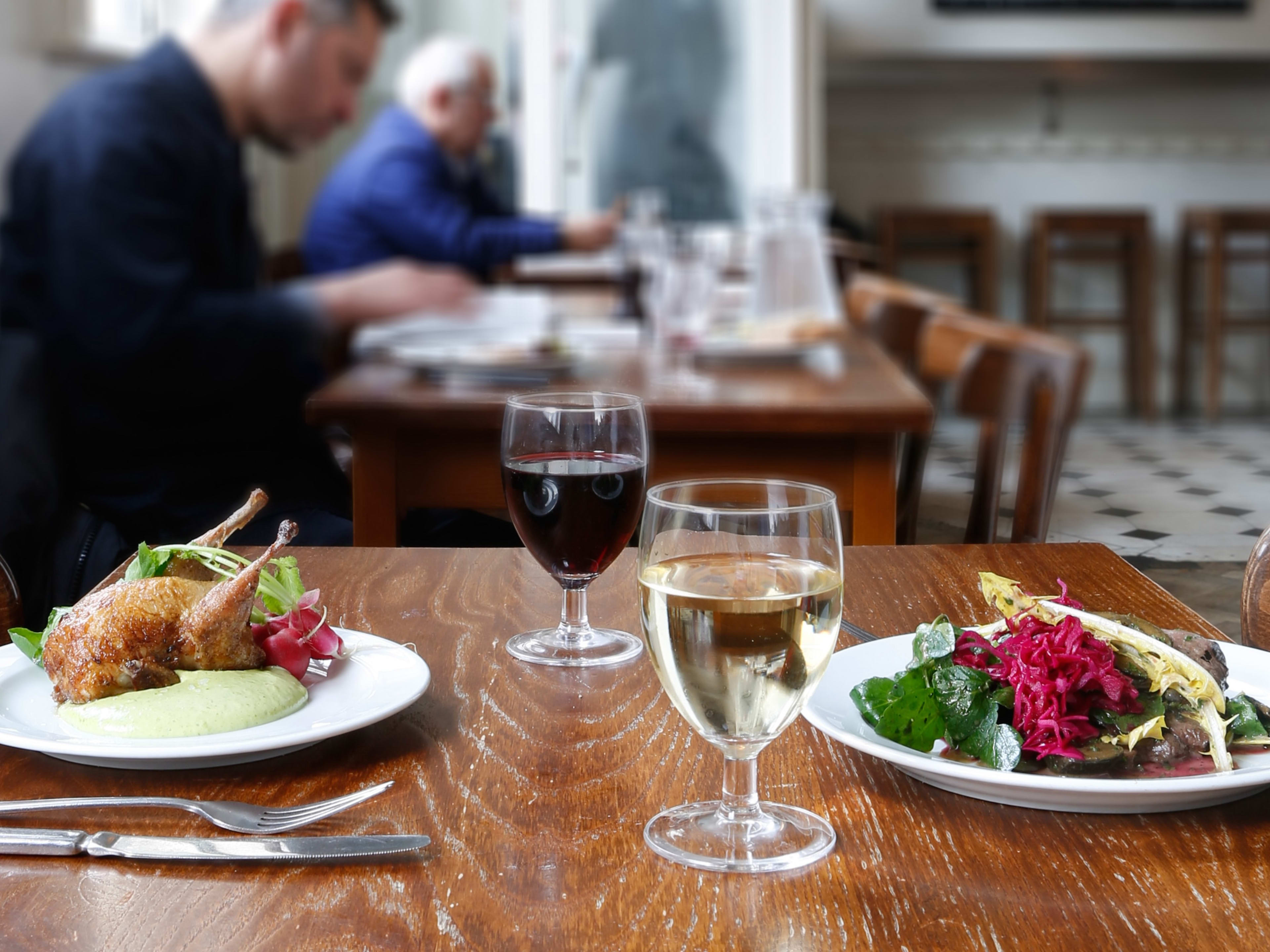 Two dishes from St. John Bread And Wine on a wooden table. People eat at other tables in the background.