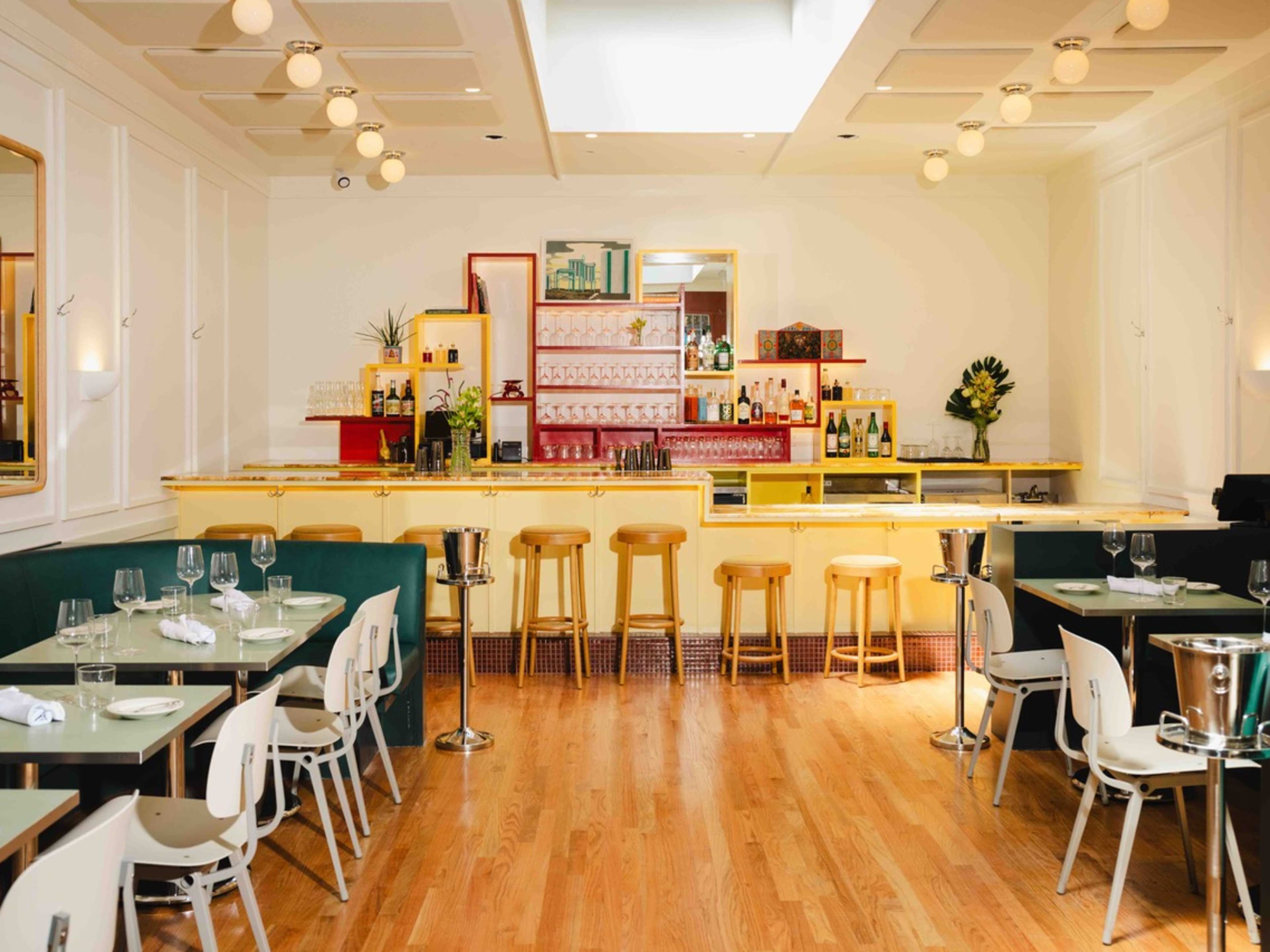 A dining room with a bar in the back and tables along the walls.