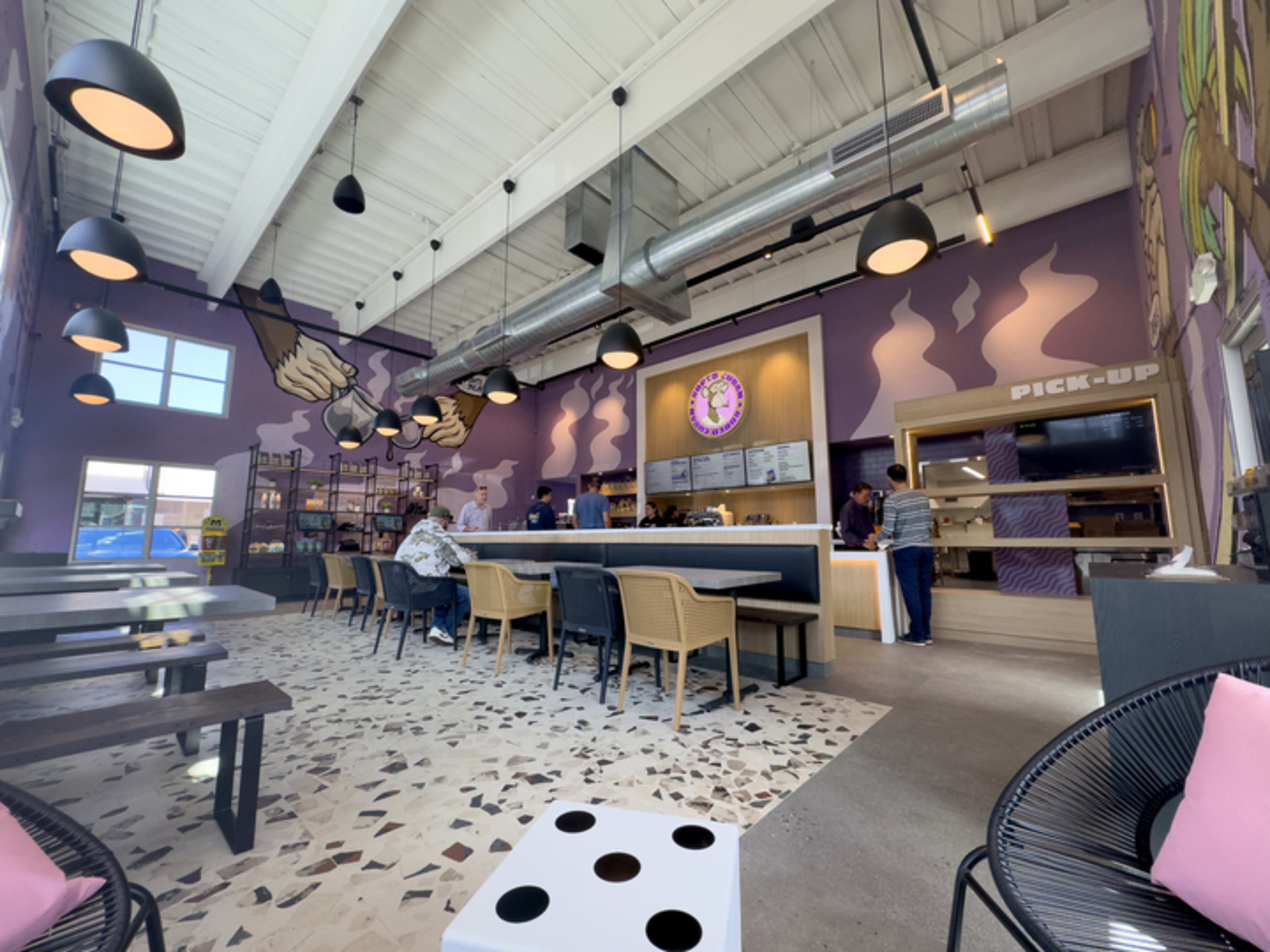 Interior of restaurant with monkey logo, purple walls, series of square tables and chairs.