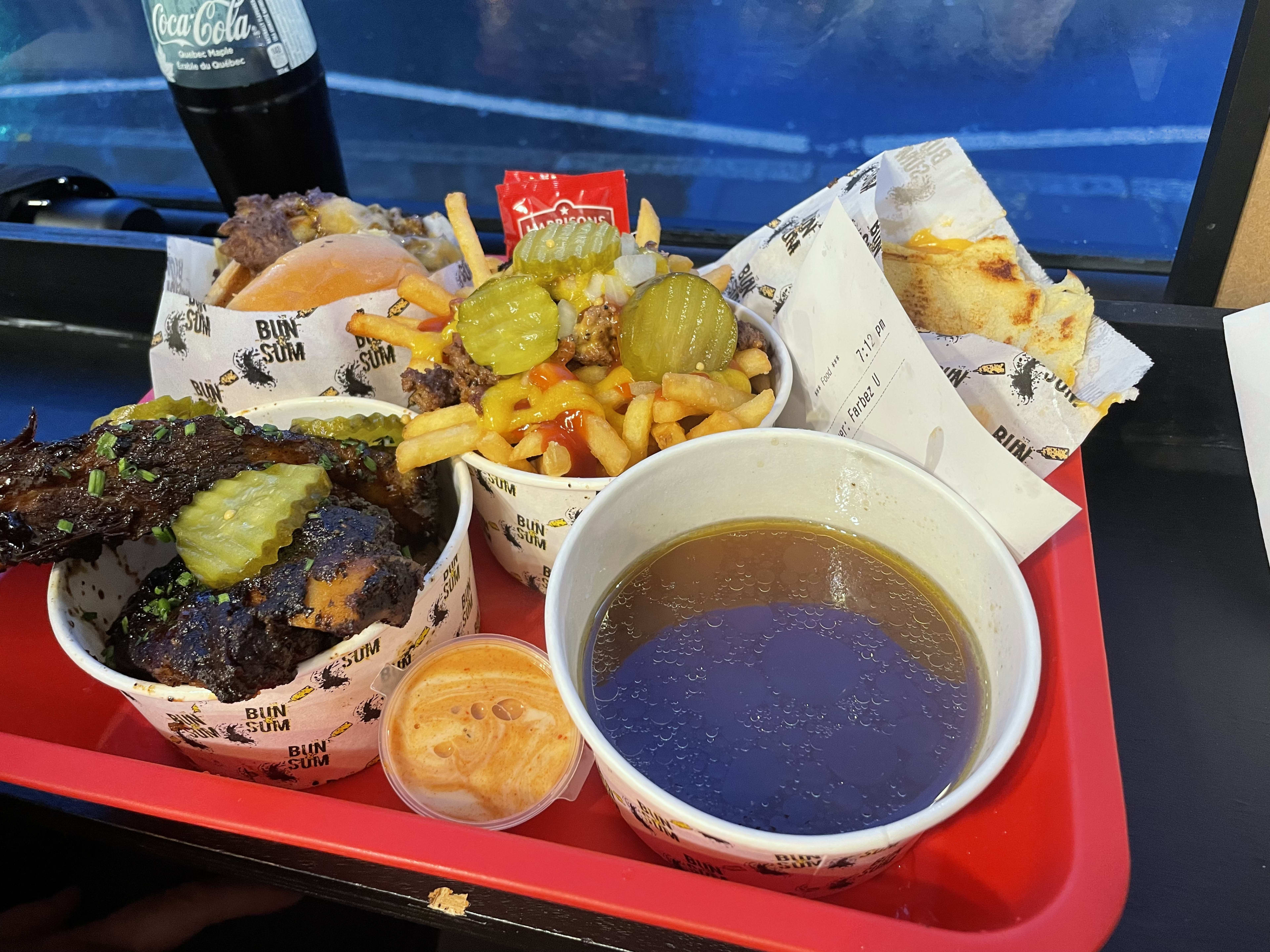 Red plastic tray containing a burger, pickle-topped frieds, ribs, and a pot of consommé.