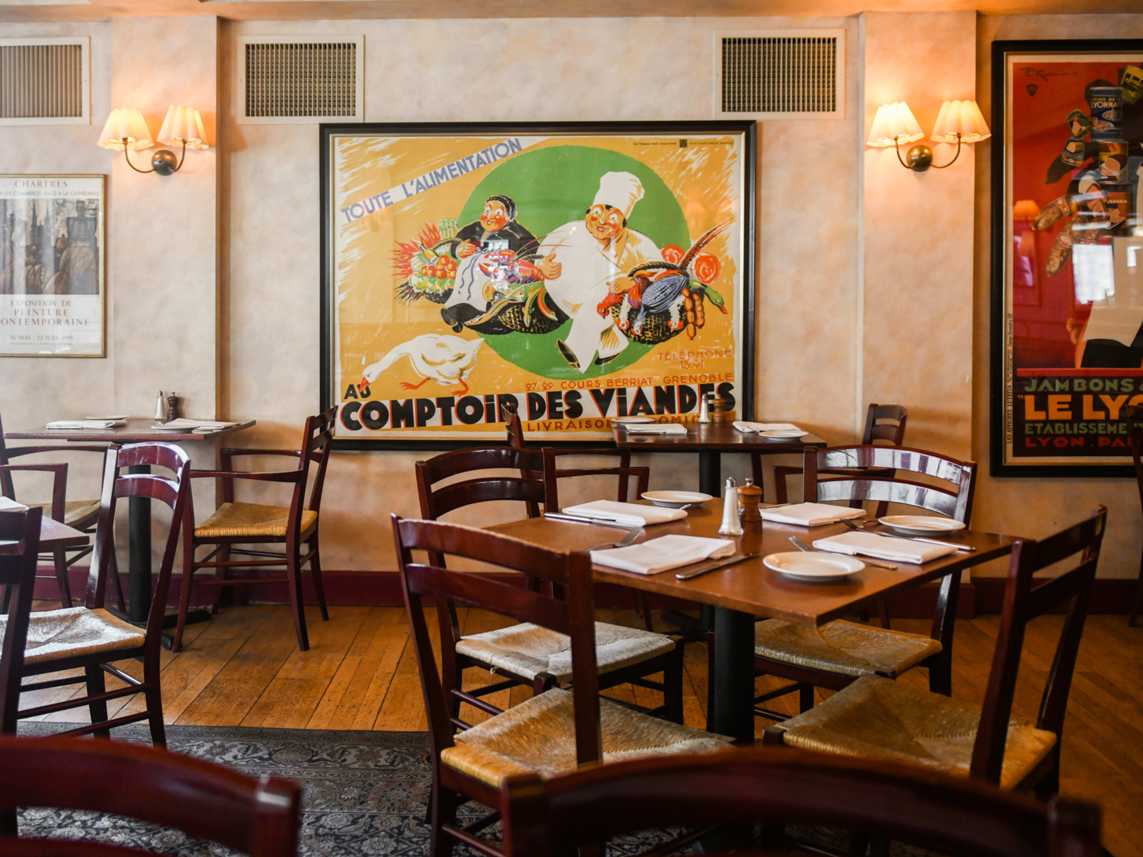 Dining room with French advertisement posters on the walls, wooden tables, and wicker chairs.