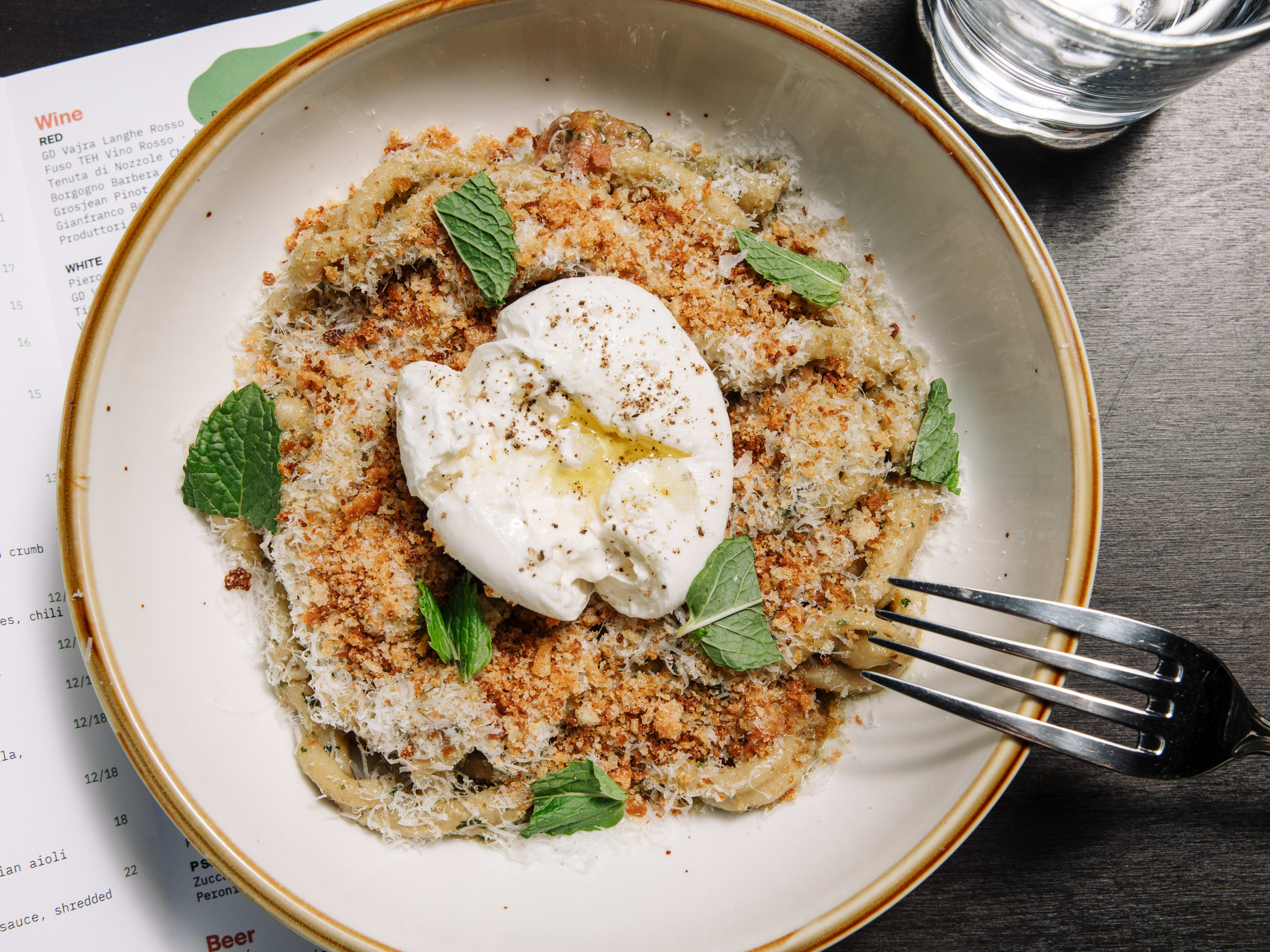 pesto pasta topped with breadcrumbs, mint leaves, and burrata