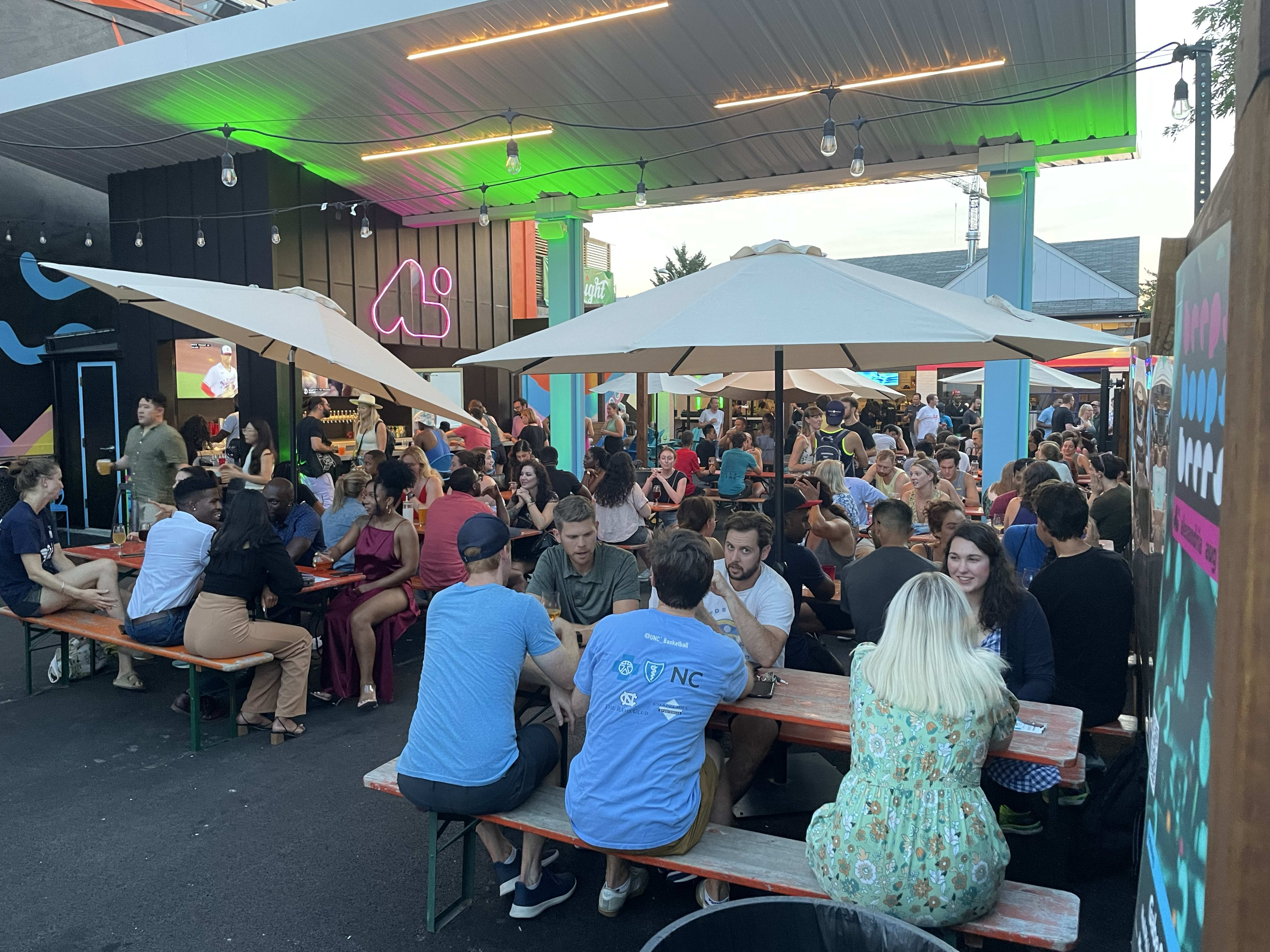 outdoor beer garden with lots of people sitting at tables under umbrellas