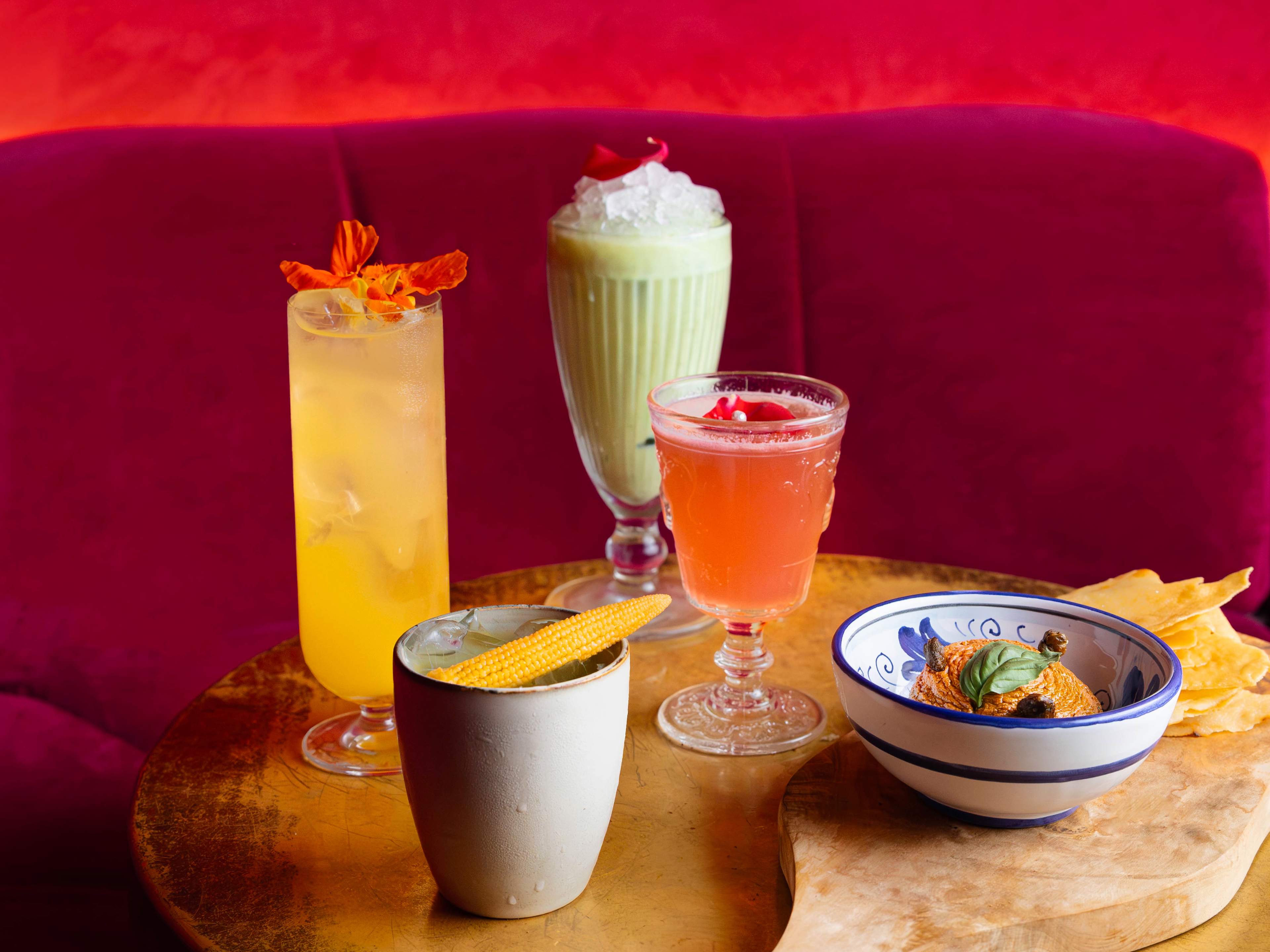 Spread of cocktails and small plates on red booth table at No Entry