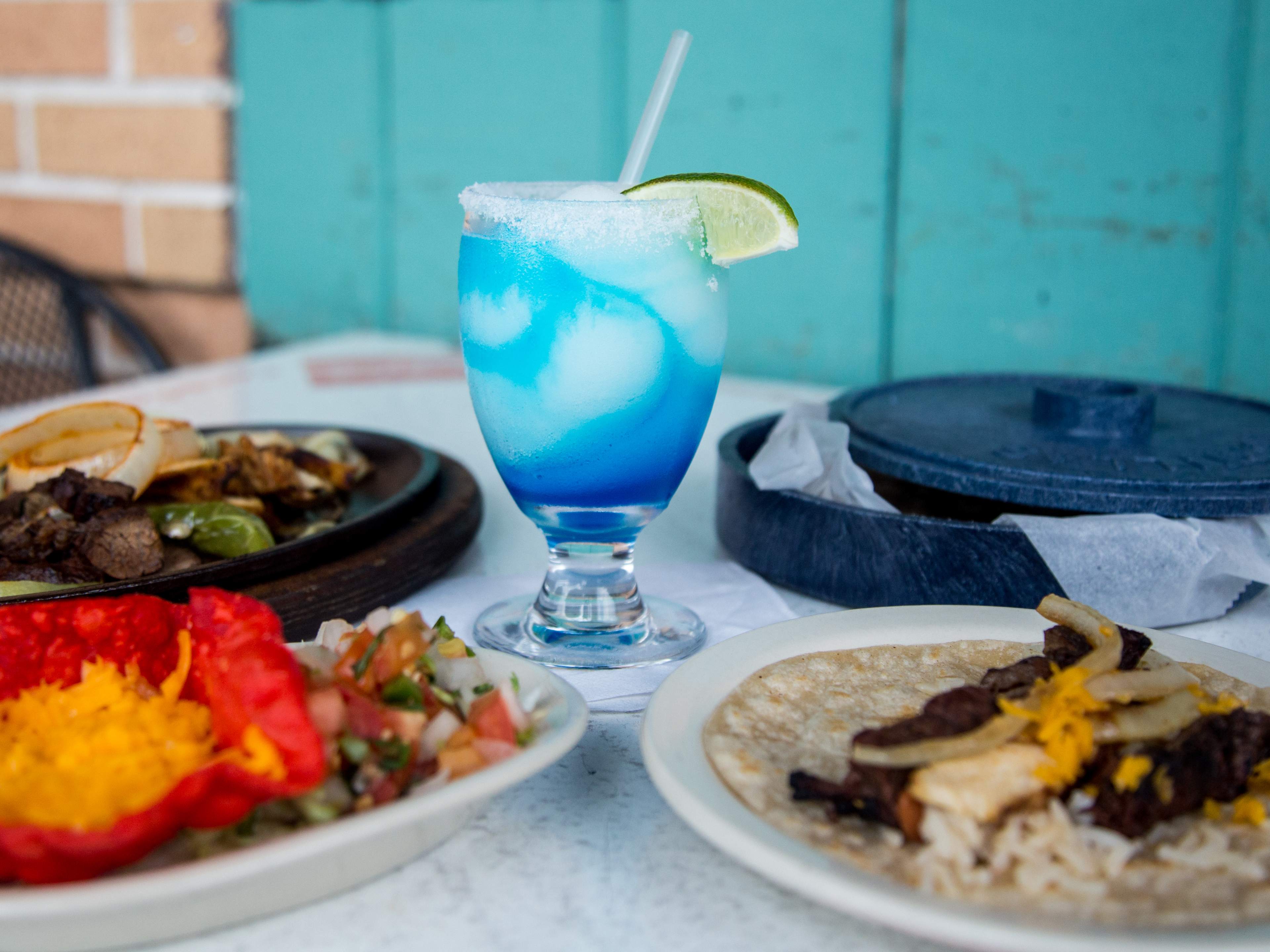 bright blue frozen margarita on a table surrounded by Tex-Mex dishes