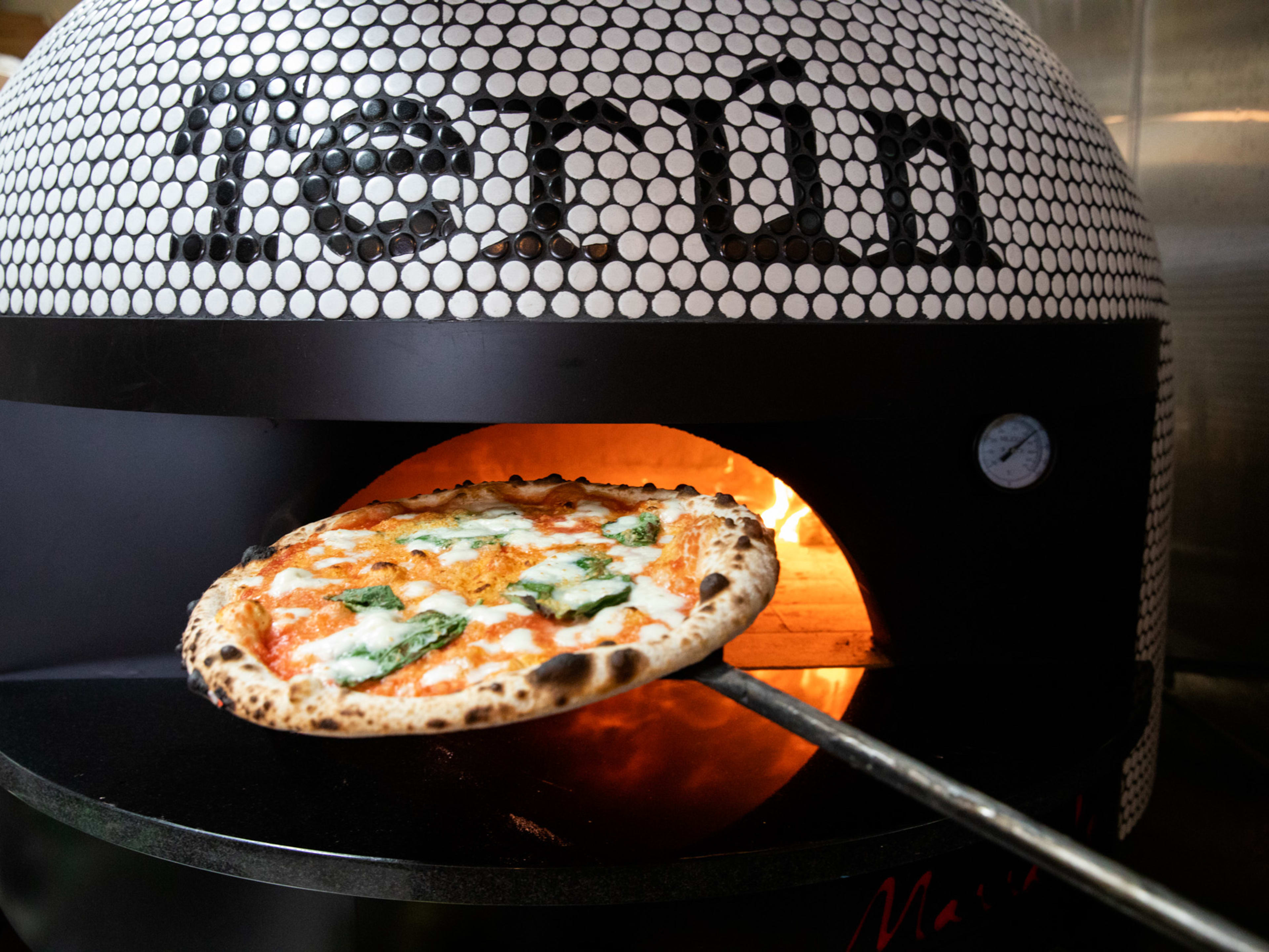 margherita pizza going into tiled pizza oven