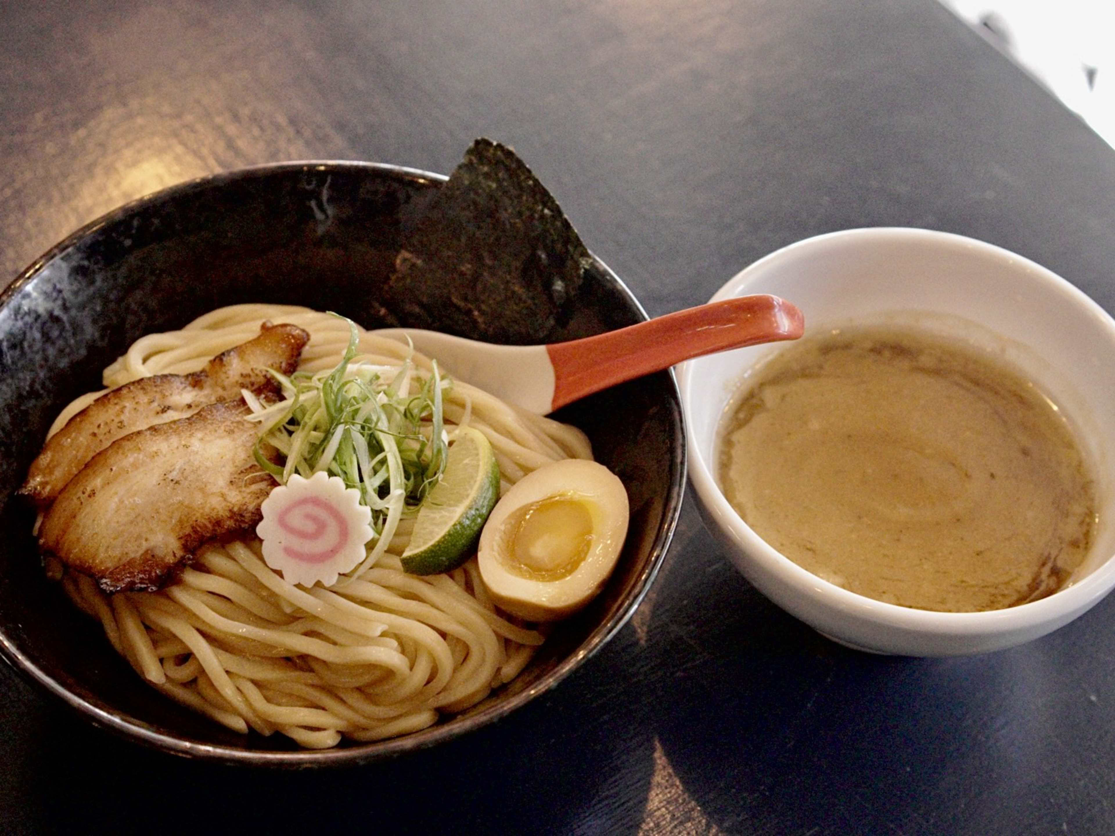 a bowl of tsukemen with chashu, naruto, lime, and a soft egg