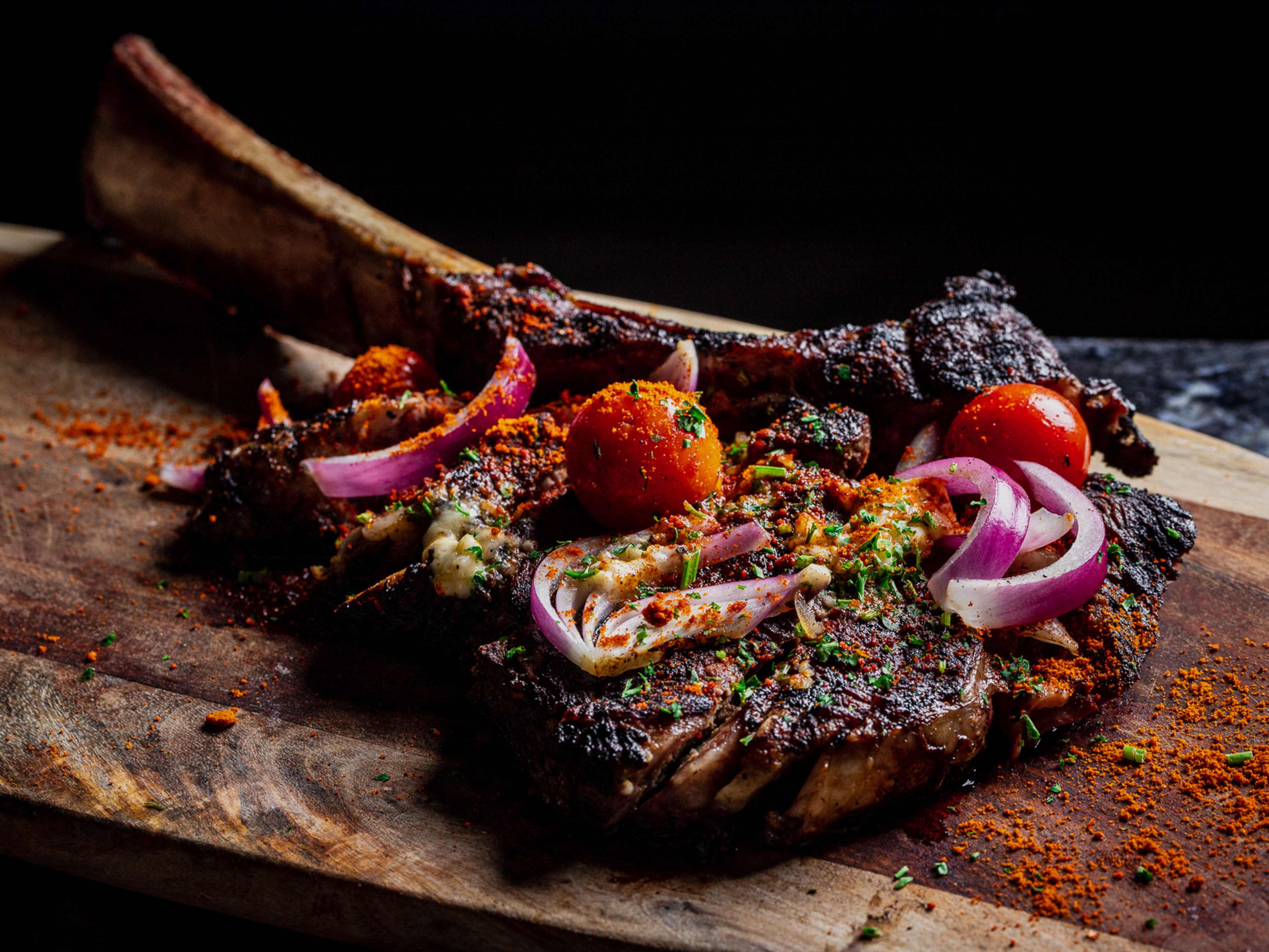 a steak on a cutting board with onions and tomatoes