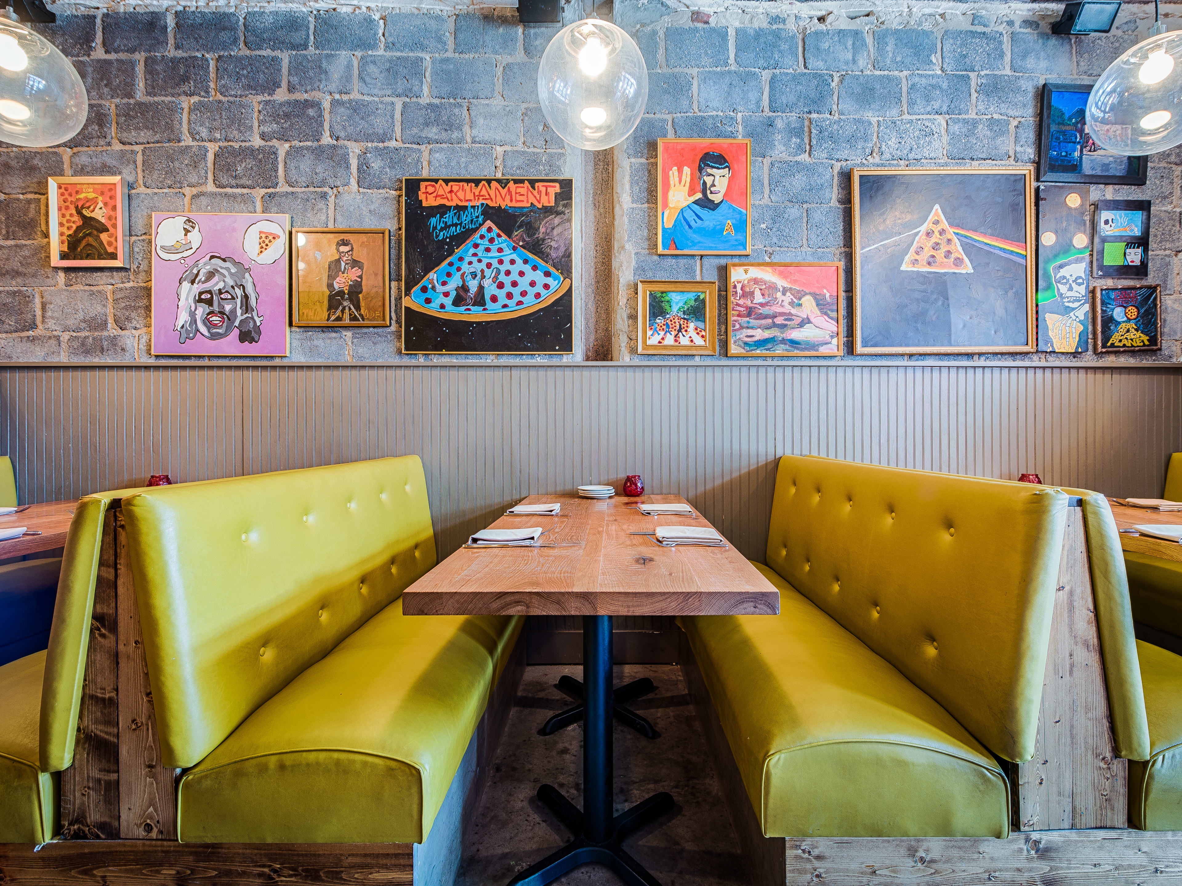 Back to back lime green booths at Little Coco's. The walls are raw concrete brick with framed artwork and hanging globe lights over each table.