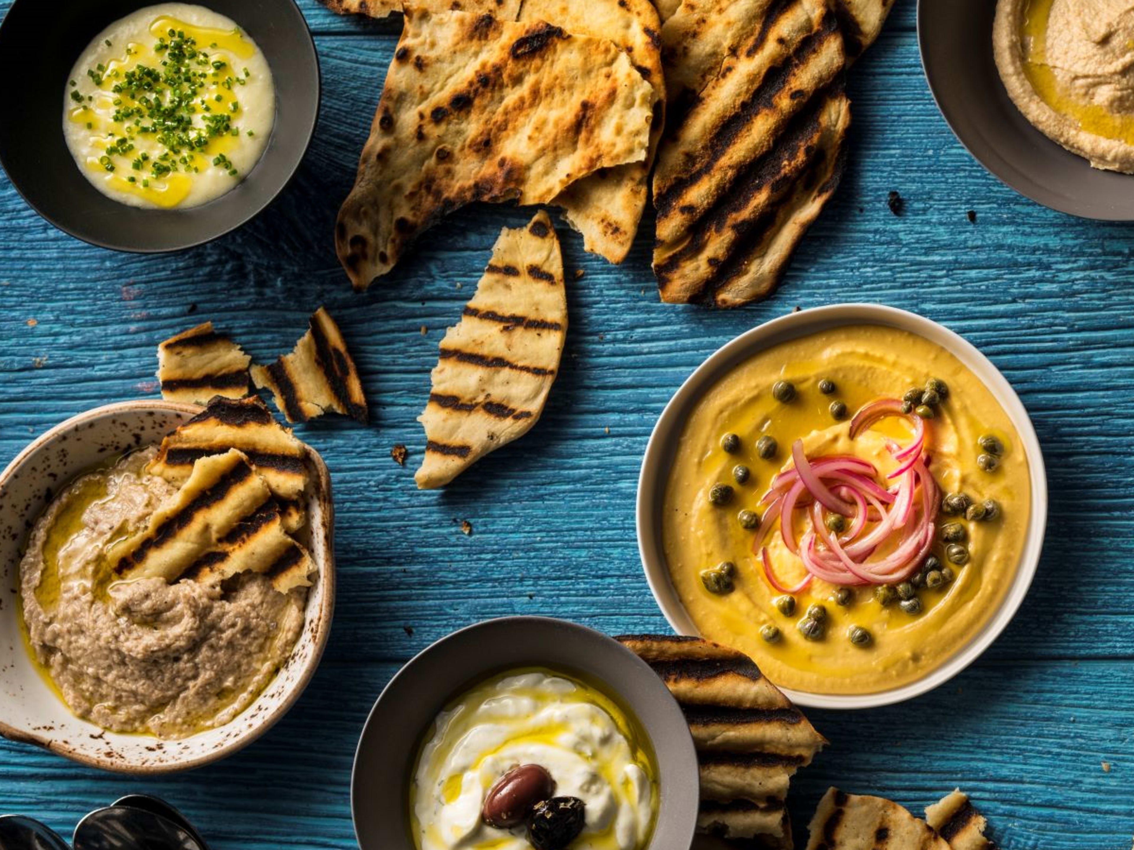 Five bowls of hummus with pita bread.